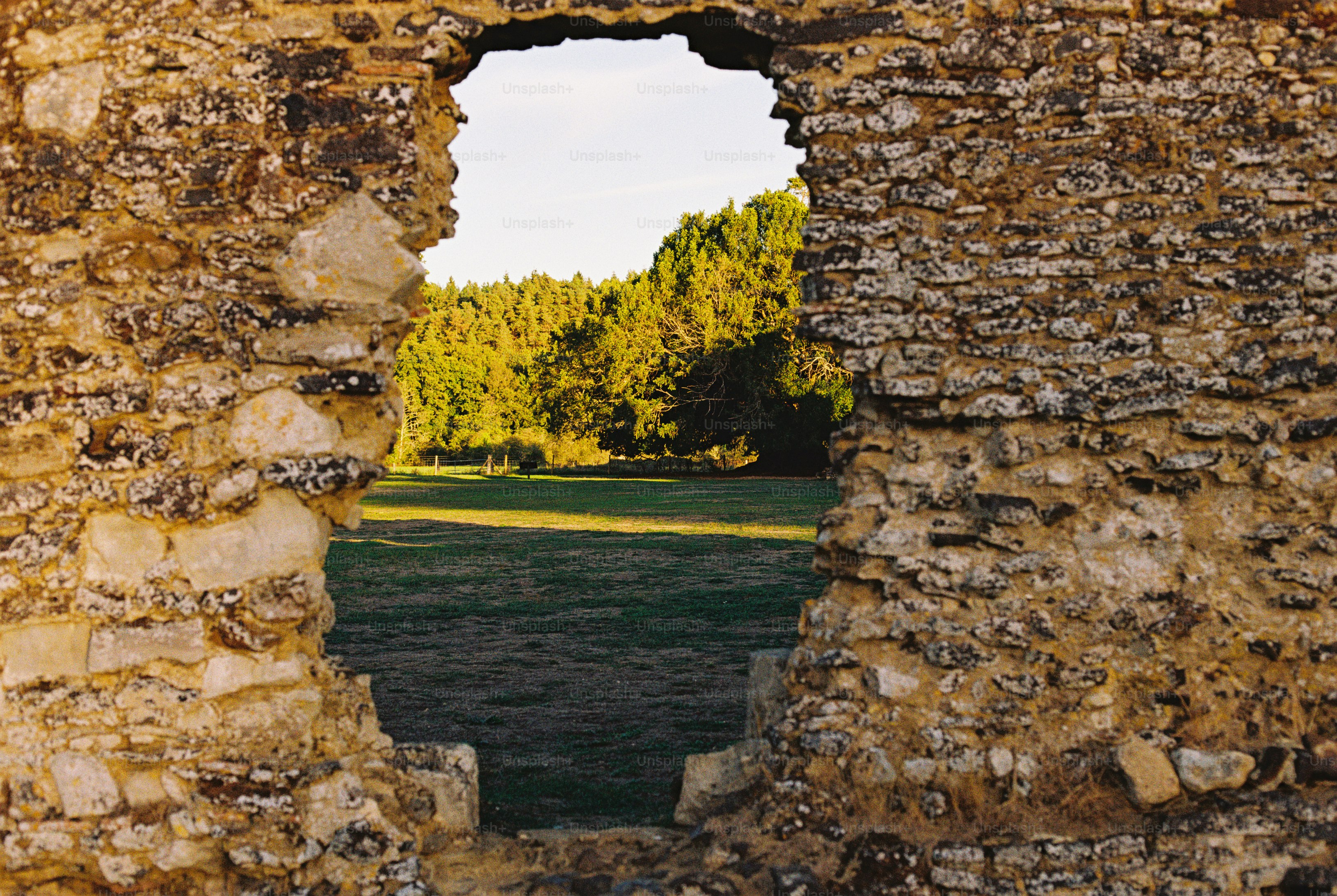 A view of a green field and trees through a hole in a stone wall
