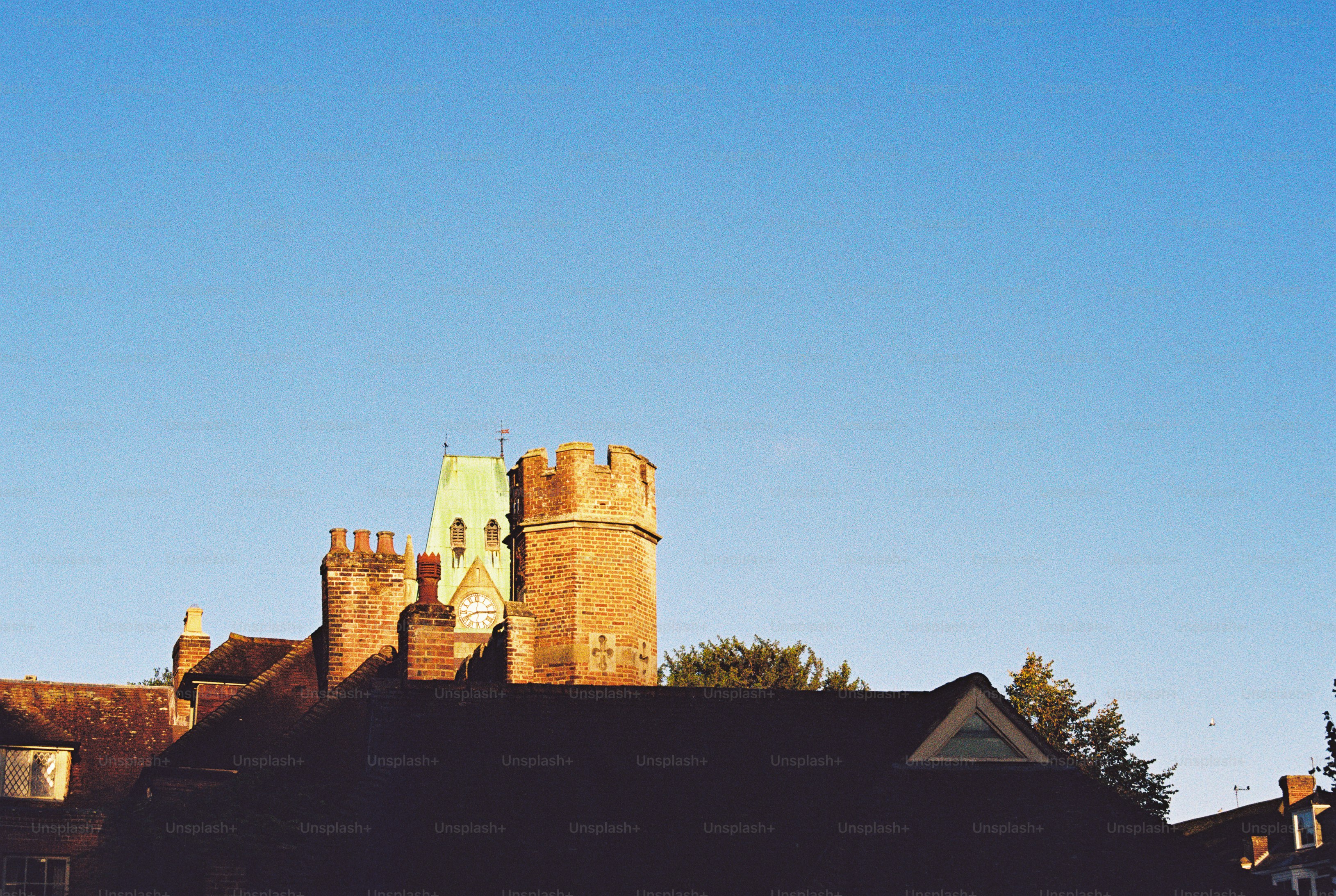A brick clock tower and roofline against a clear blue sky in golden hour light