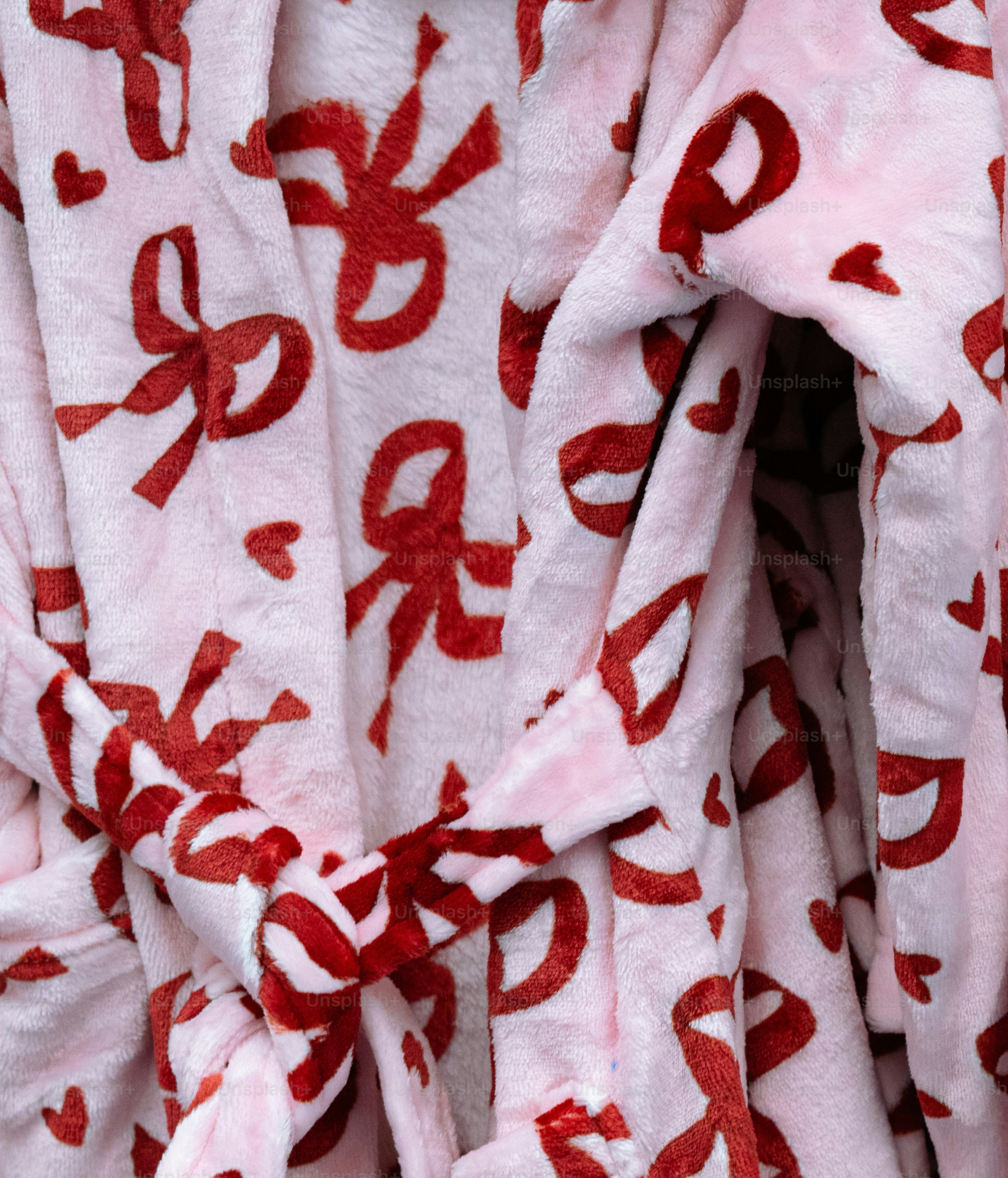 A soft pink plush bathrobe with a repeating pattern of red bows and hearts