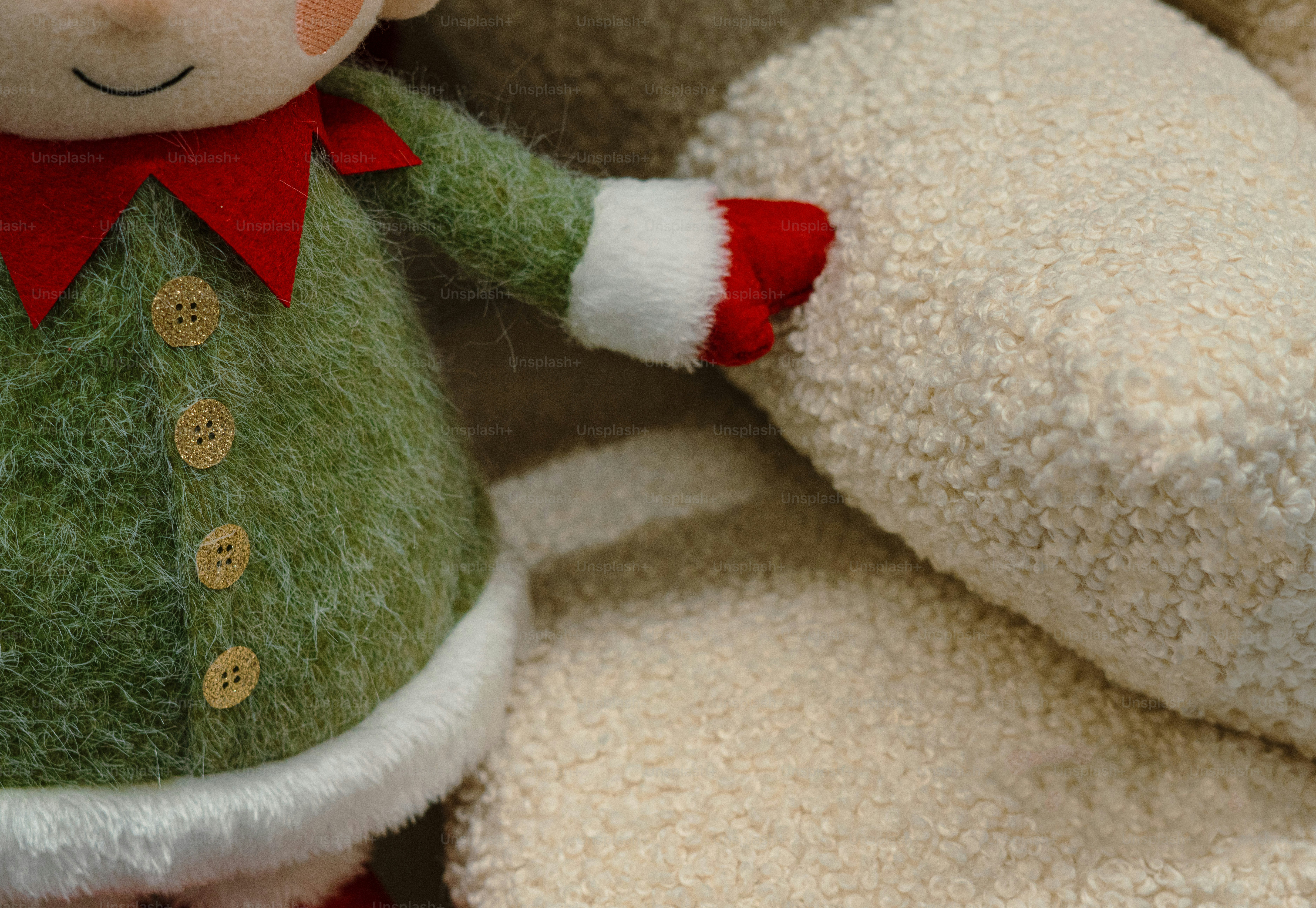 A felt elf doll in a green coat with gold buttons beside a textured cream cushion