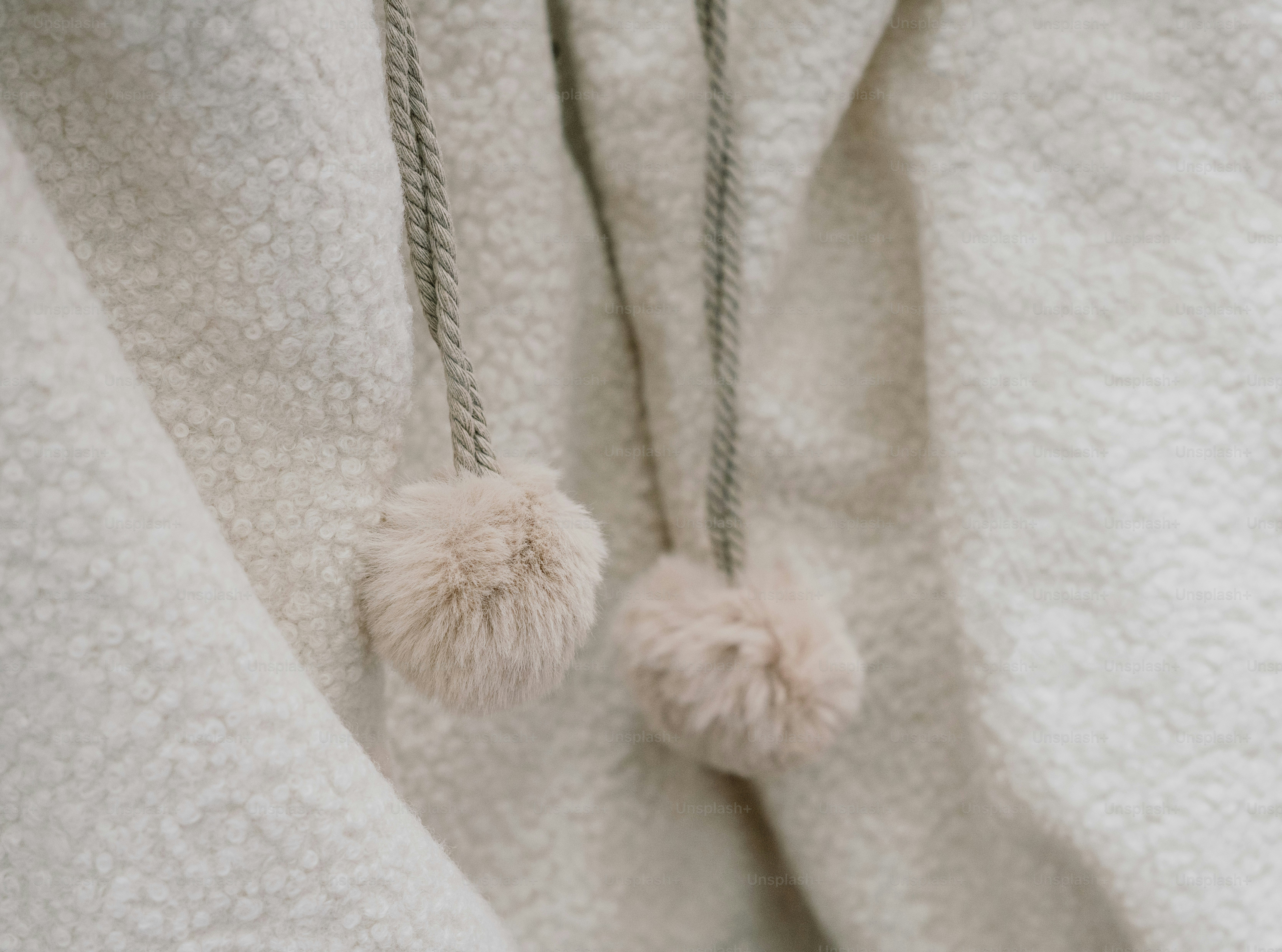 Two fluffy pom-poms hanging from braided drawstrings on a textured cream fleece garment