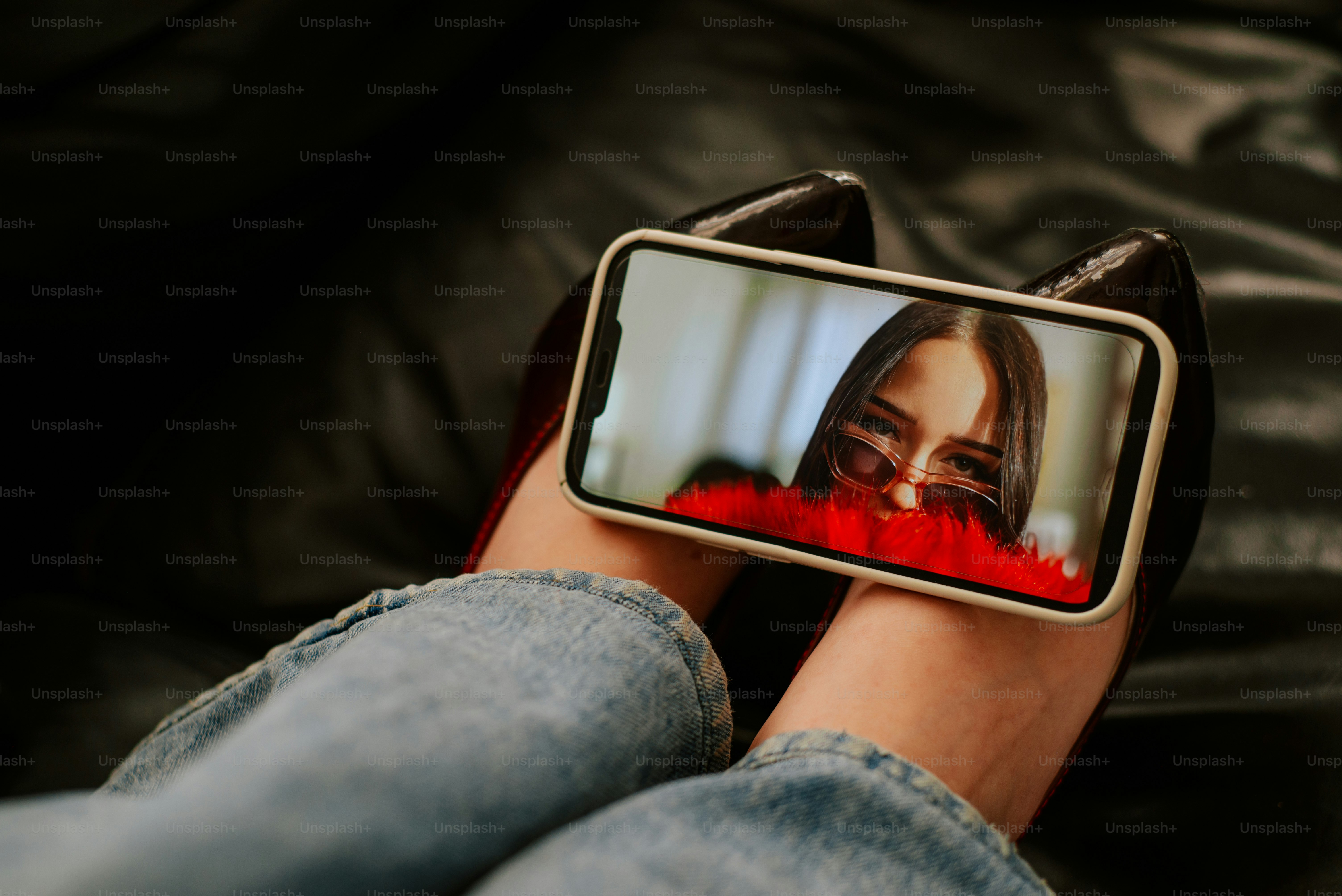 A smartphone displaying a portrait of a woman wearing sunglasses resting on a person's lap