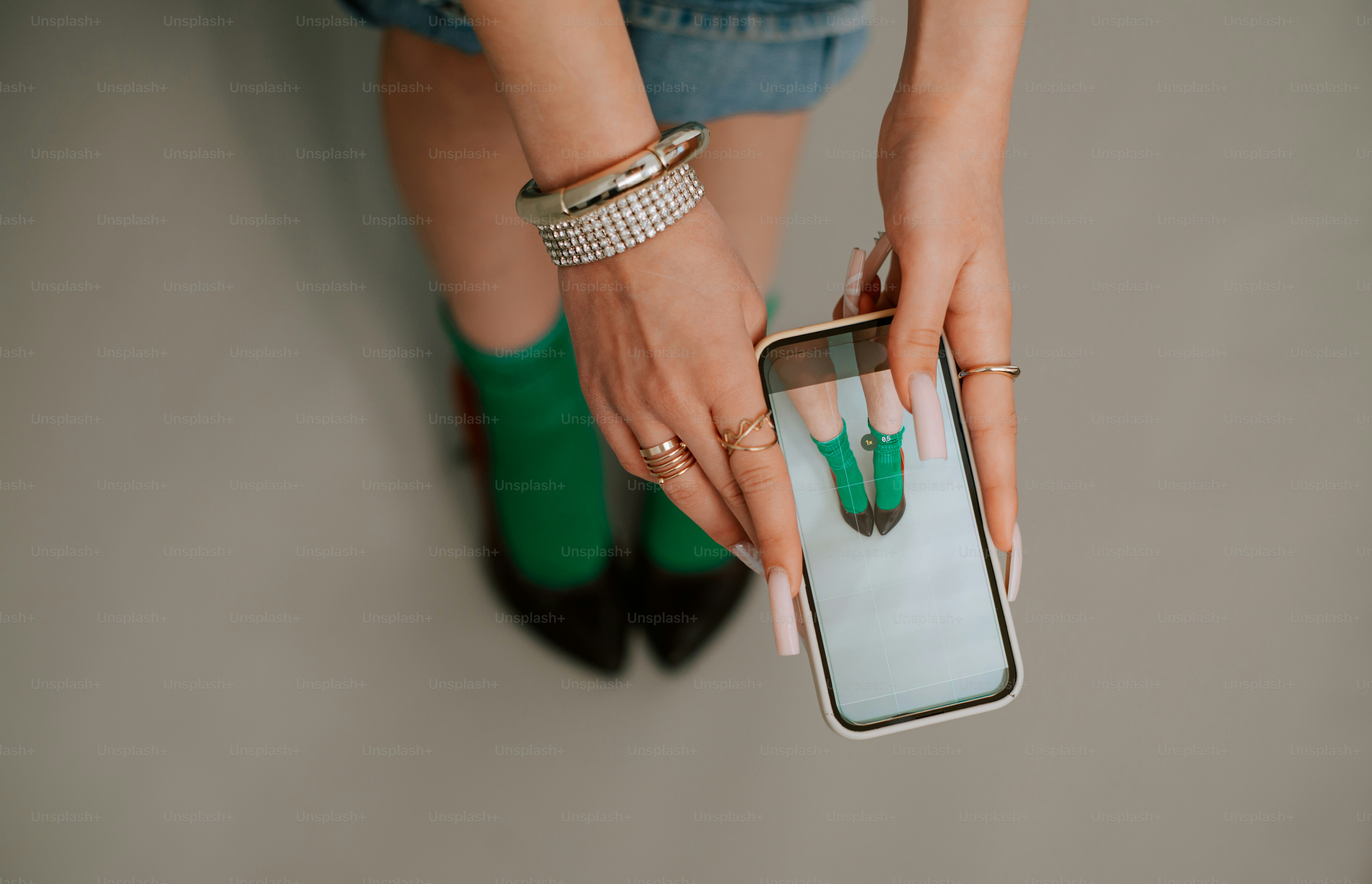 A person holding a smartphone to photograph their own feet in green socks and black heels