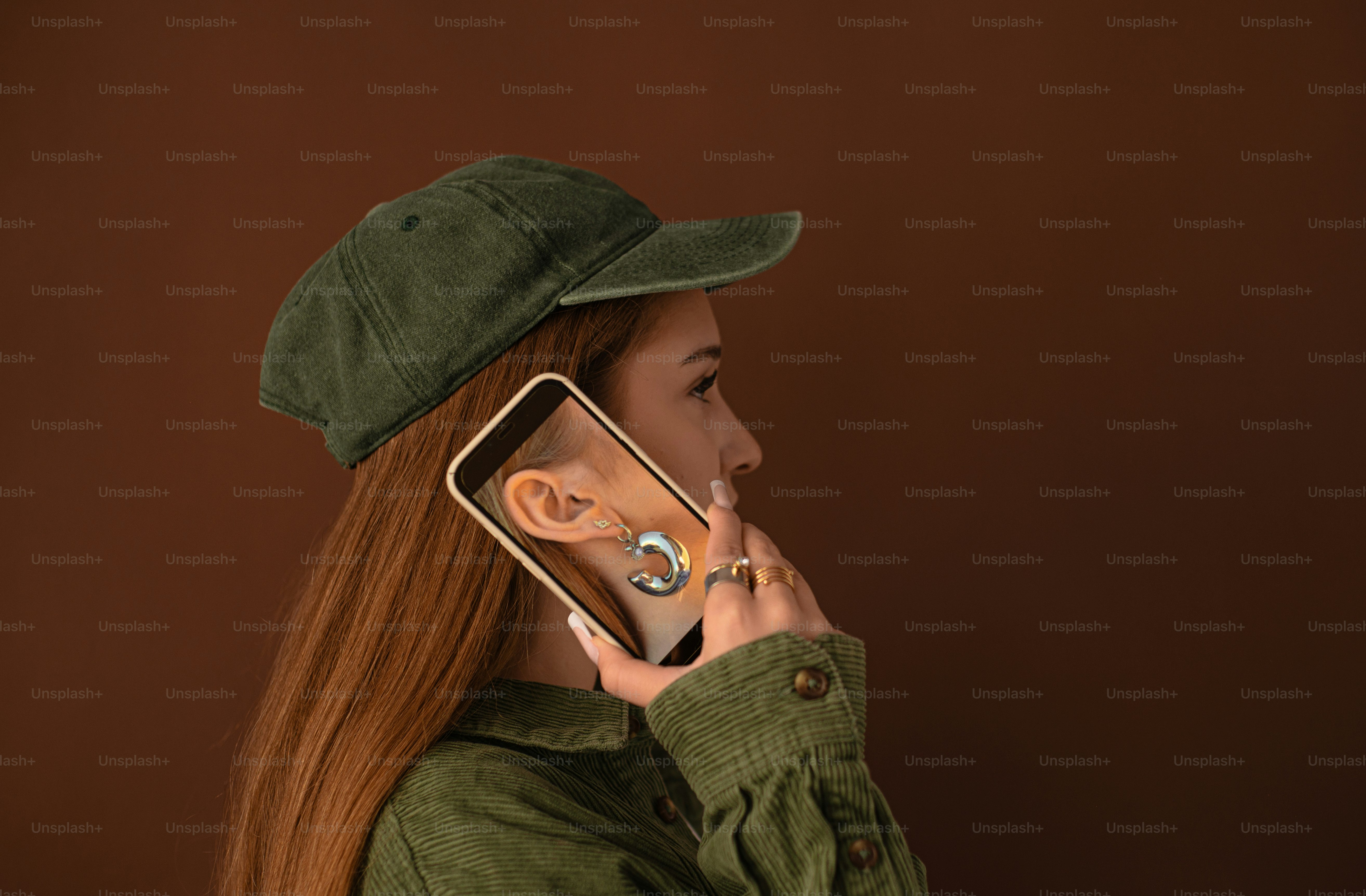 A person in a green cap and shirt holding a phone displaying an ear with a silver earring