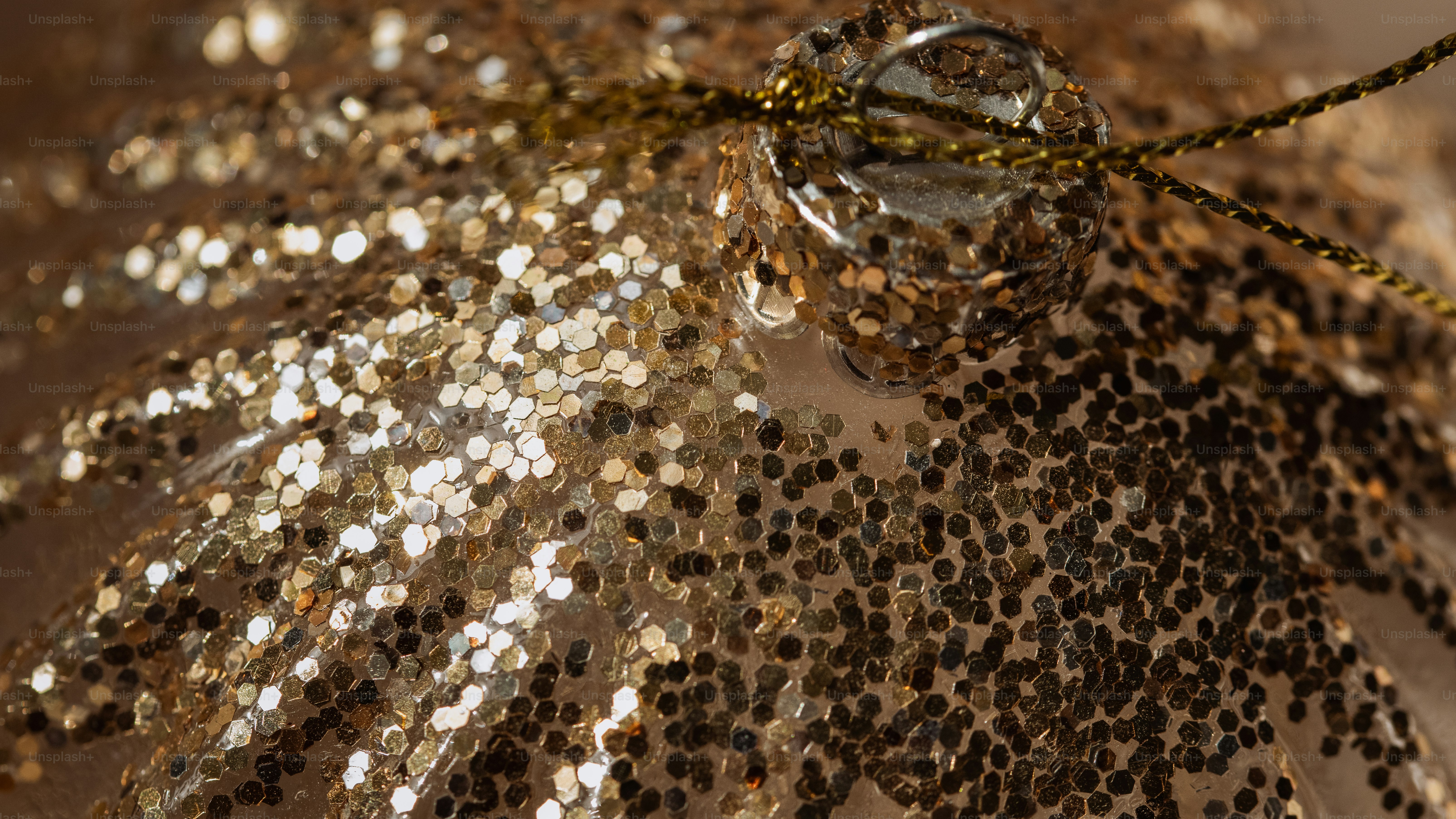 A close-up of a gold glitter Christmas ornament with a metallic cap and gold string
