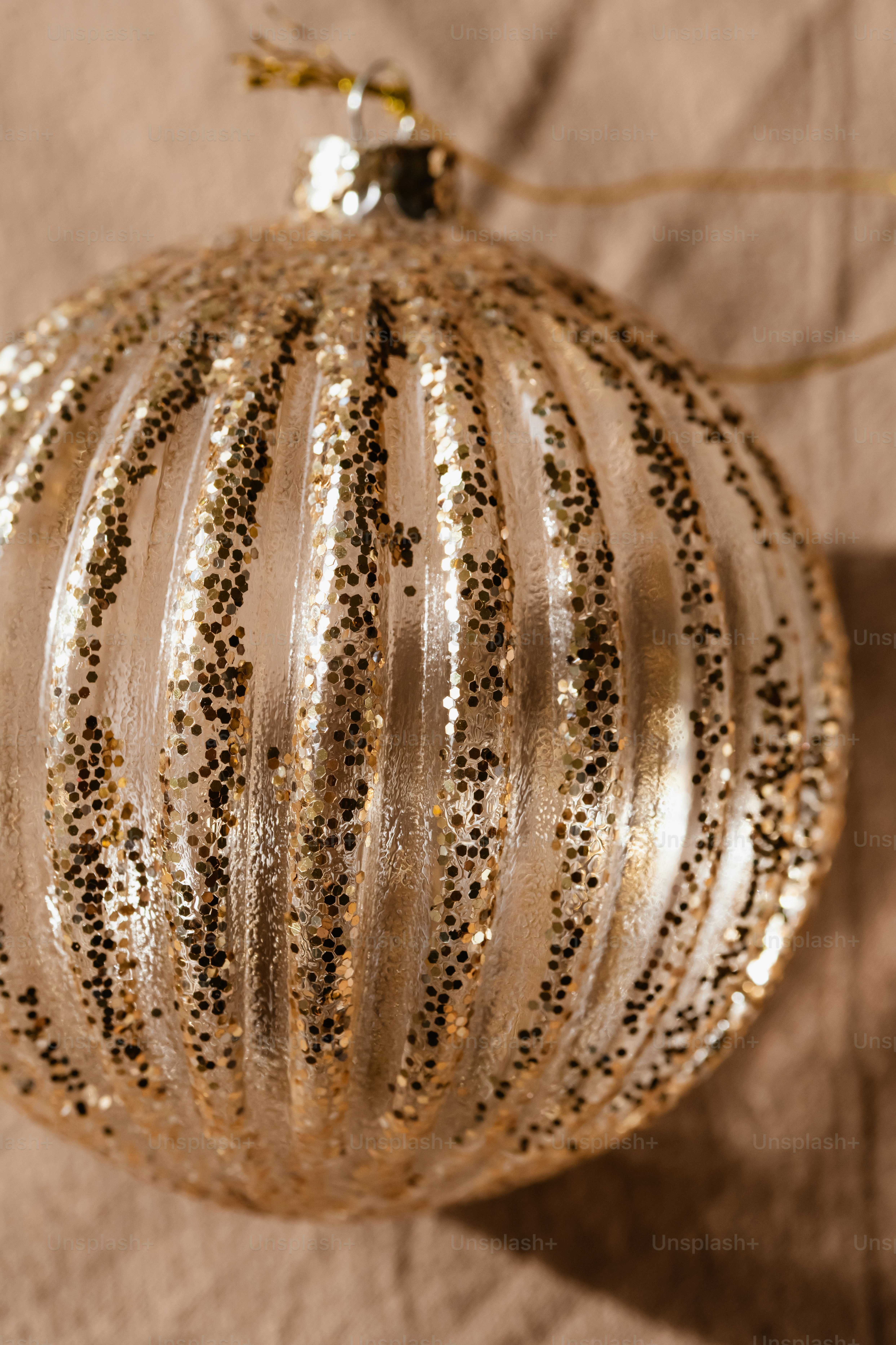 A ribbed gold Christmas ornament covered in sparkling glitter against a textured beige background