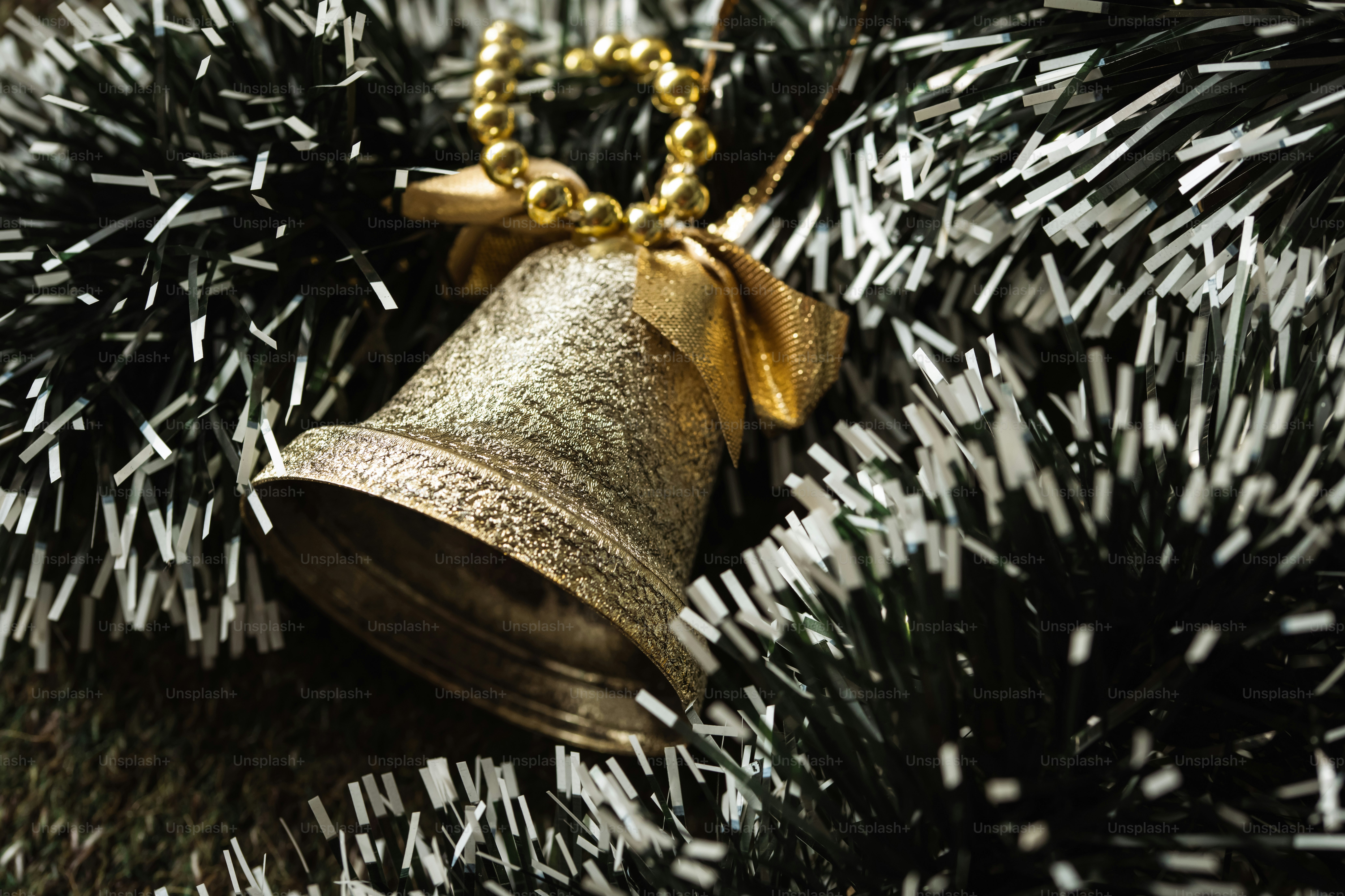 A textured gold bell with a bow hanging in dark green tinsel