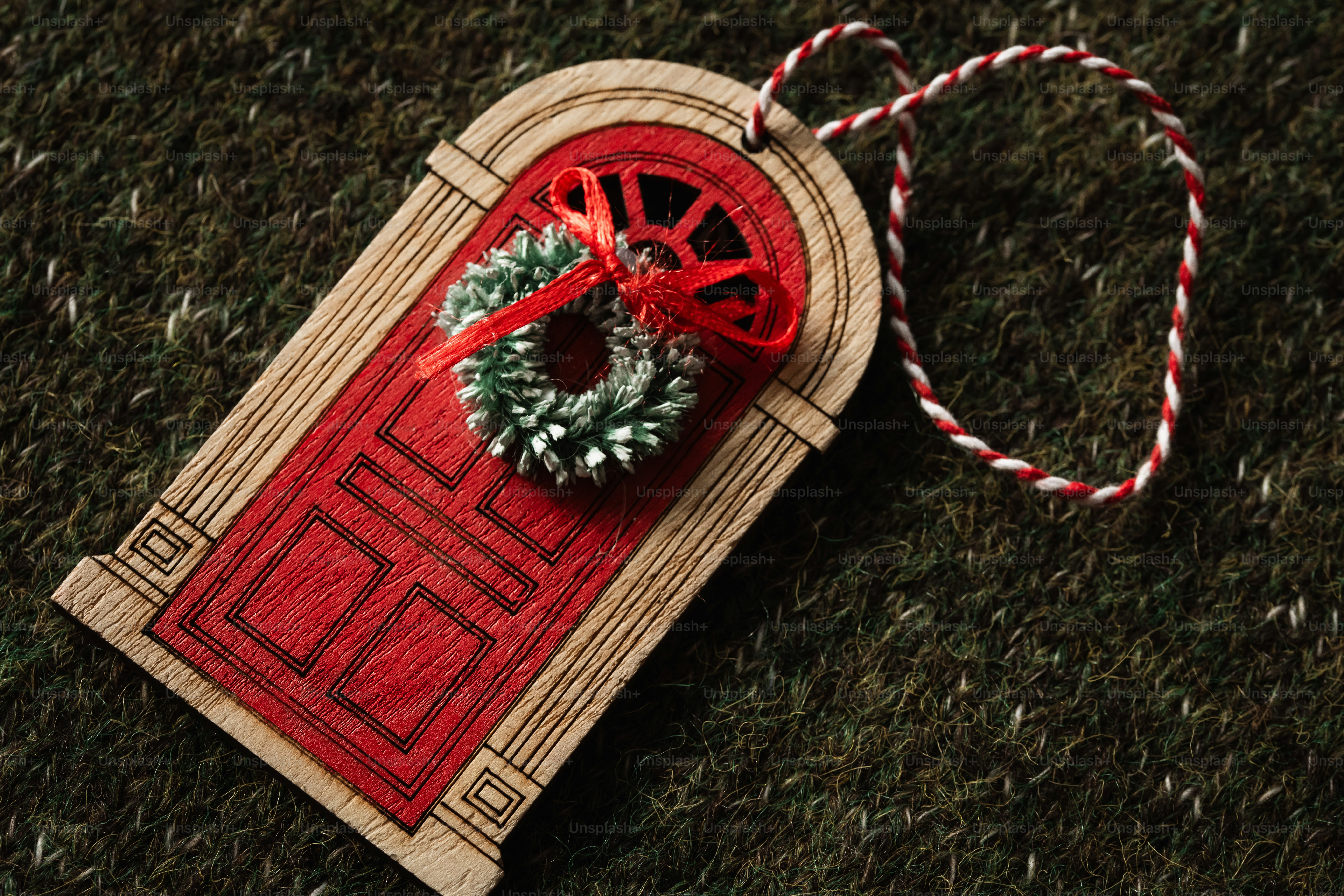 A wooden door ornament with a small wreath and red bow on a green textured surface