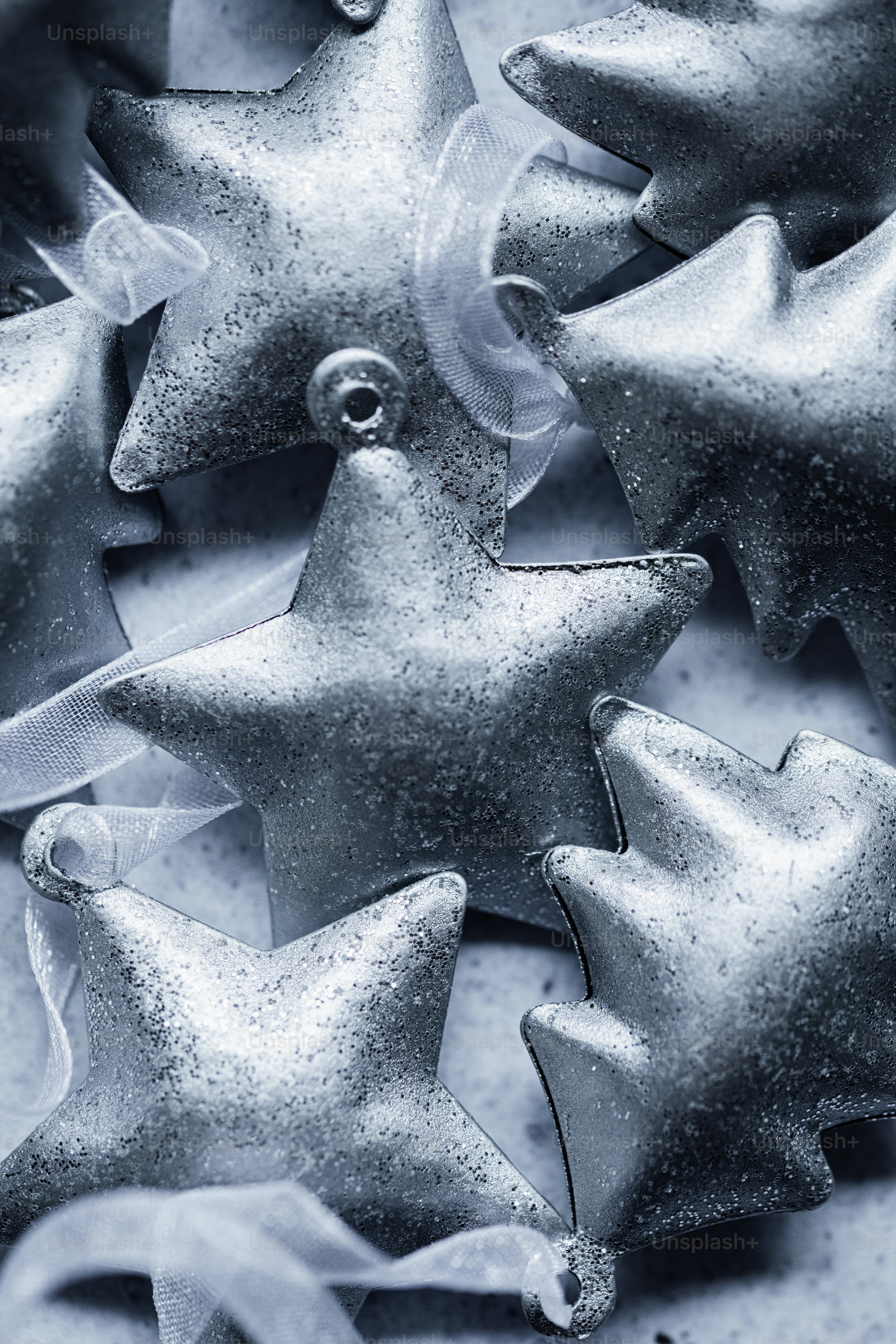 Silver glittery star ornaments with sheer ribbons arranged in a festive pile