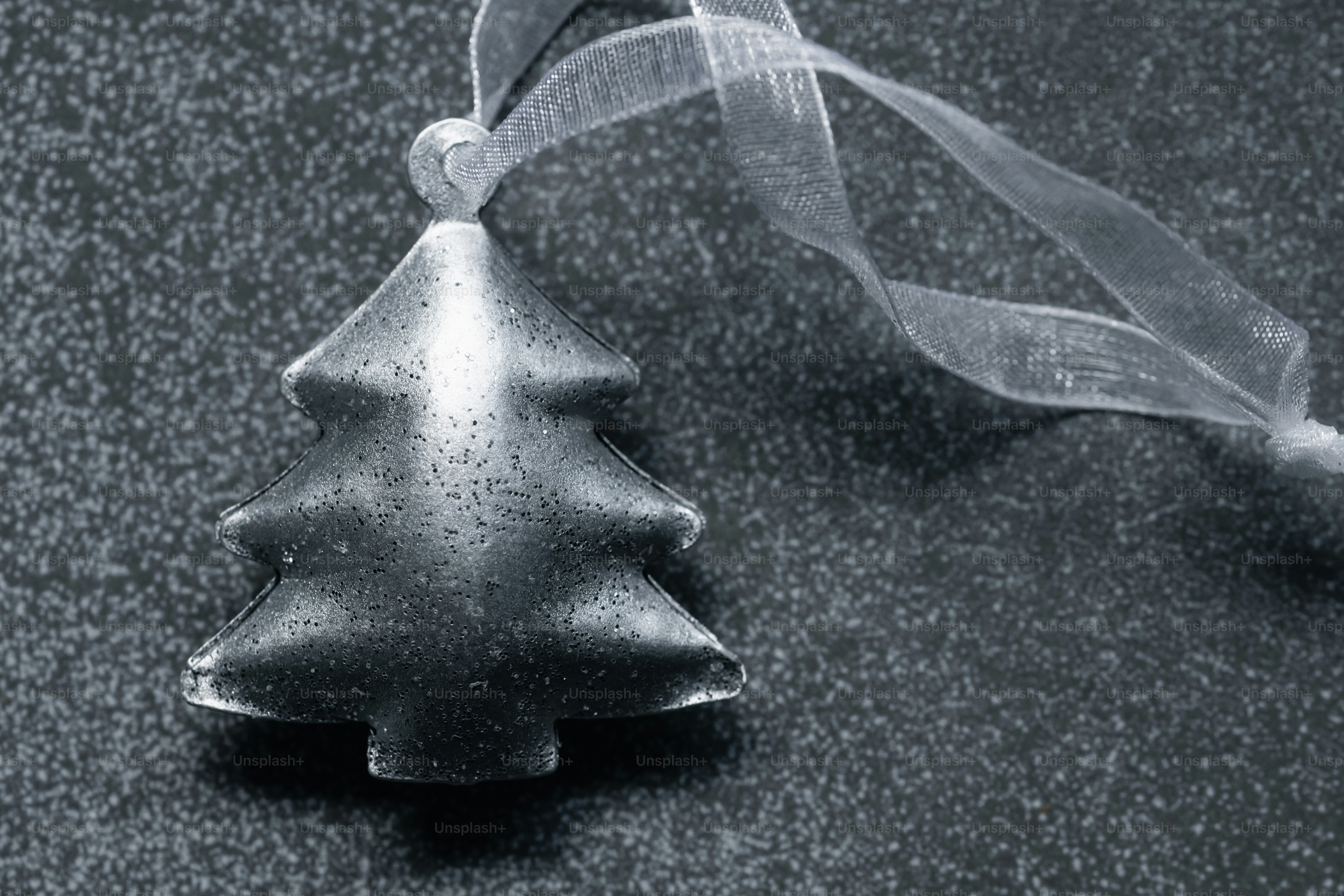 A silver Christmas tree ornament with a ribbon against a dark textured background