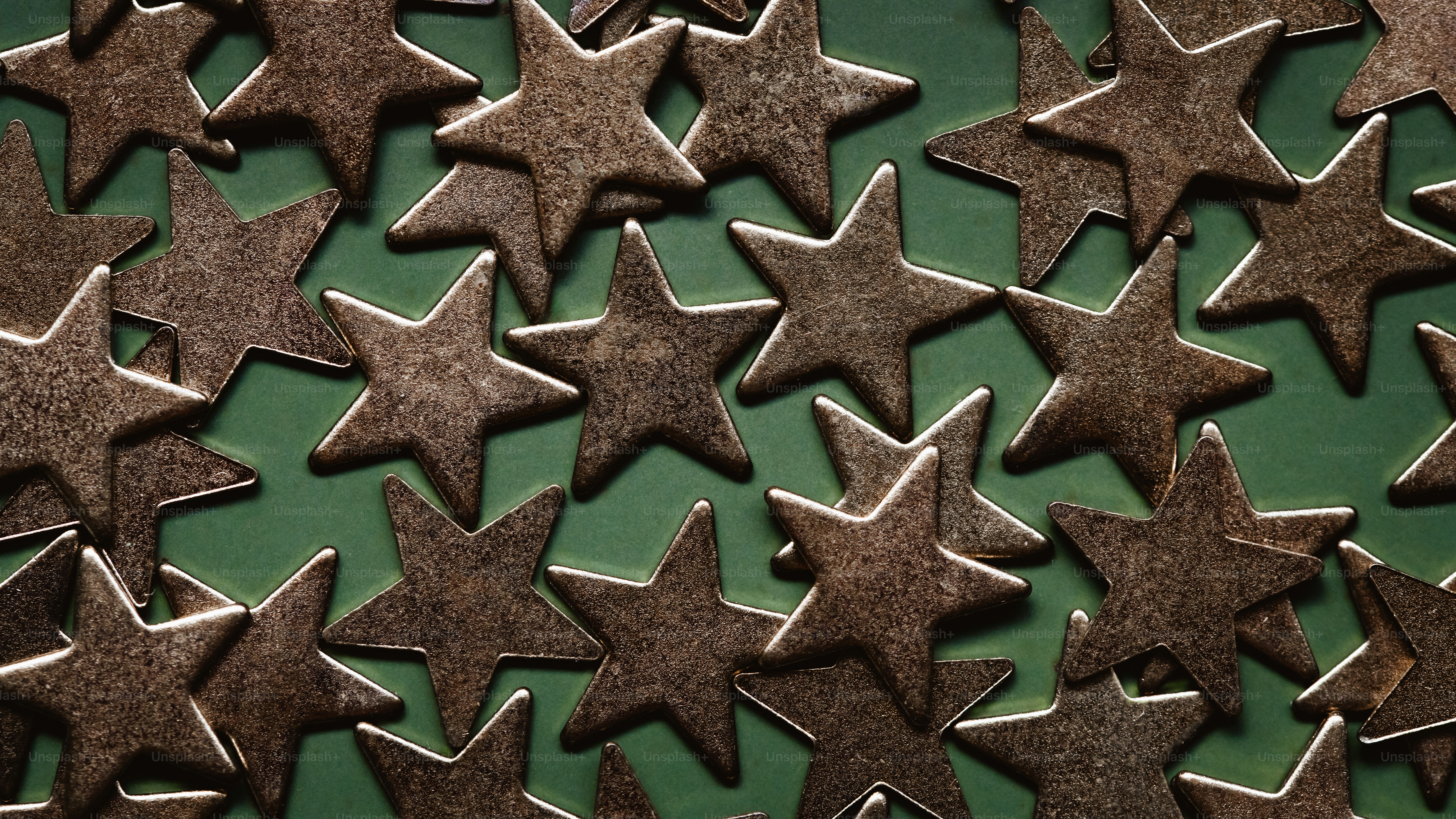 A scatter of metallic bronze star shapes on a solid green background