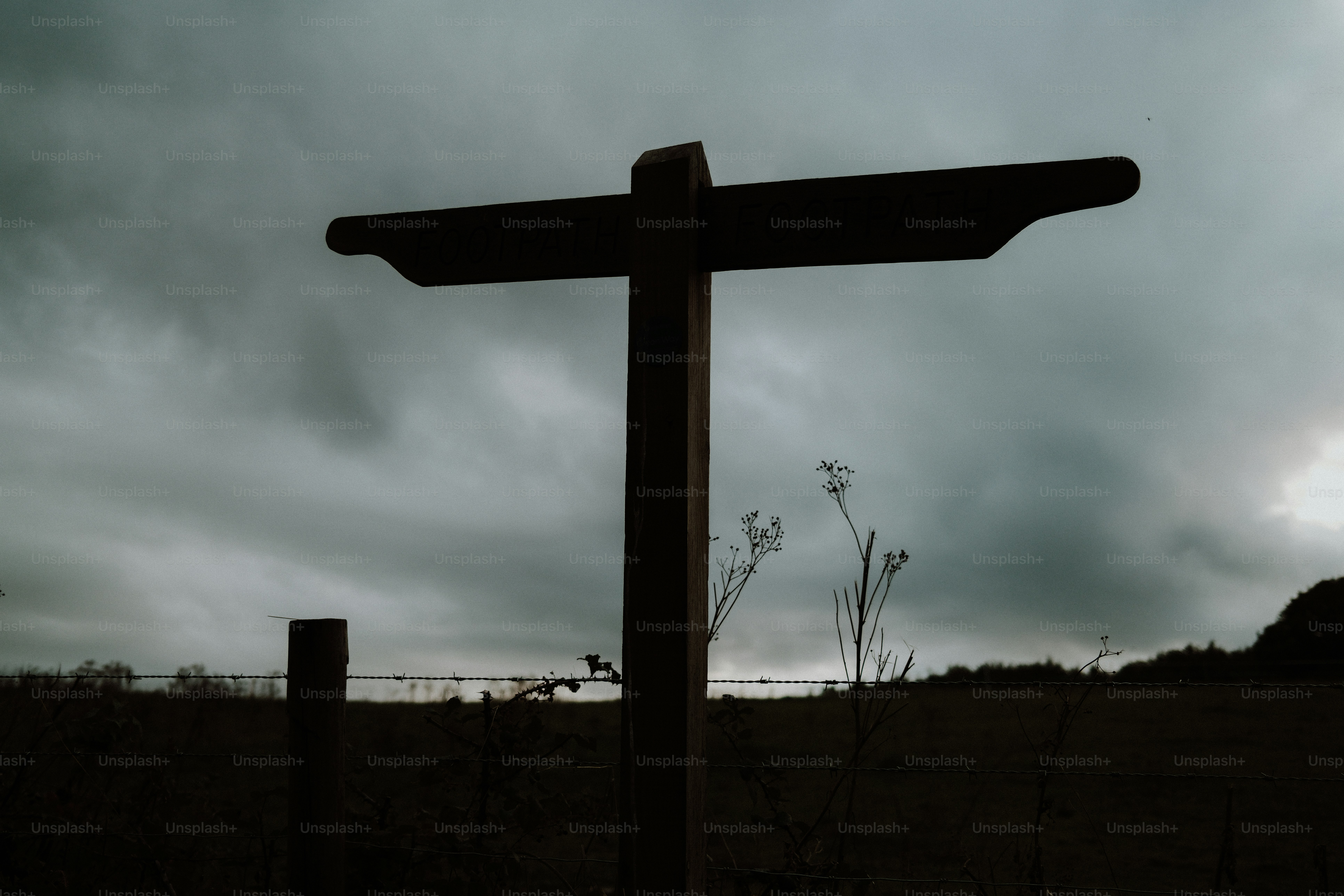 A wooden signpost in silhouette against a dark, overcast sky in a field