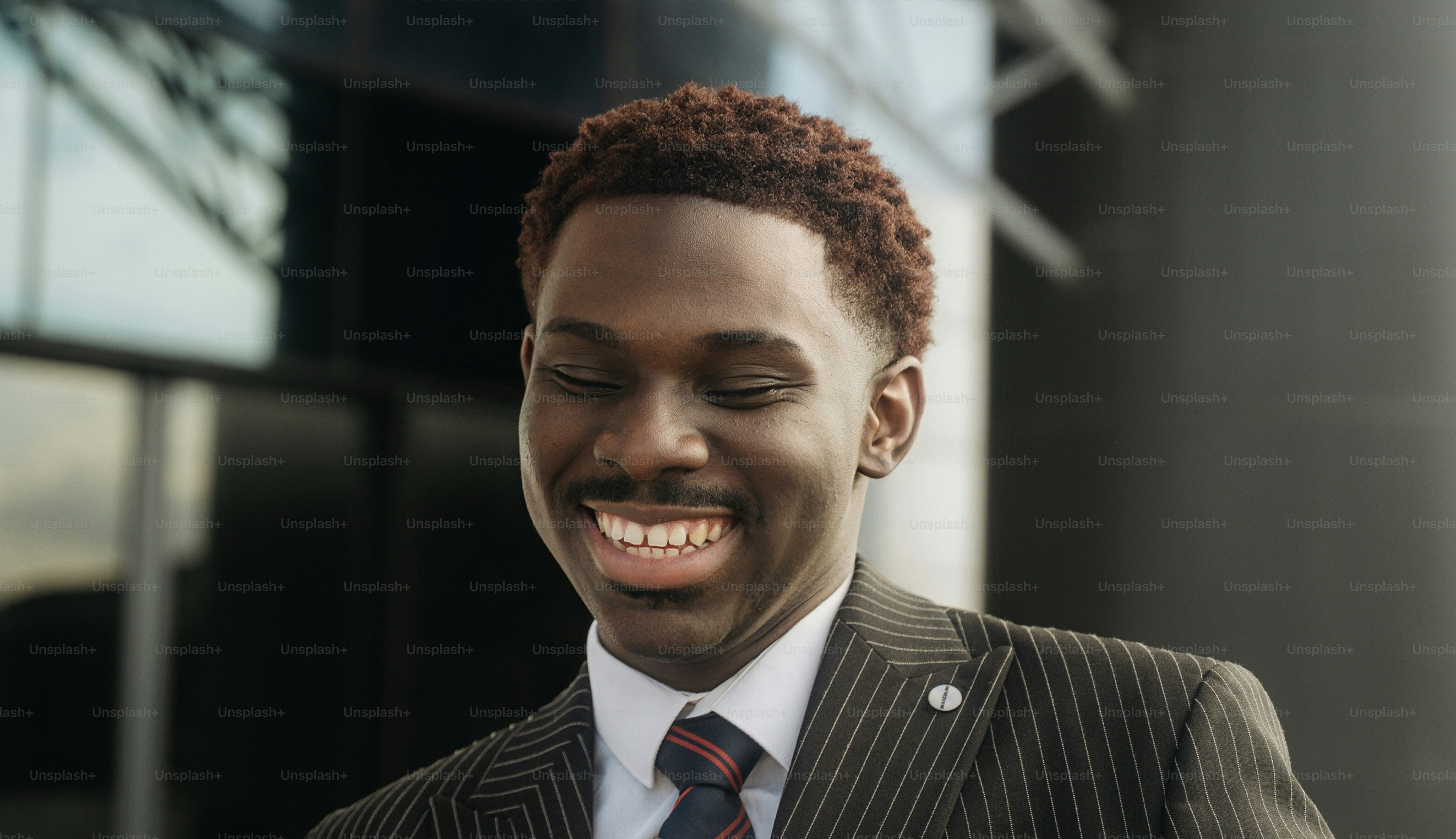 A smiling man with short reddish-brown hair in a pinstriped suit and tie