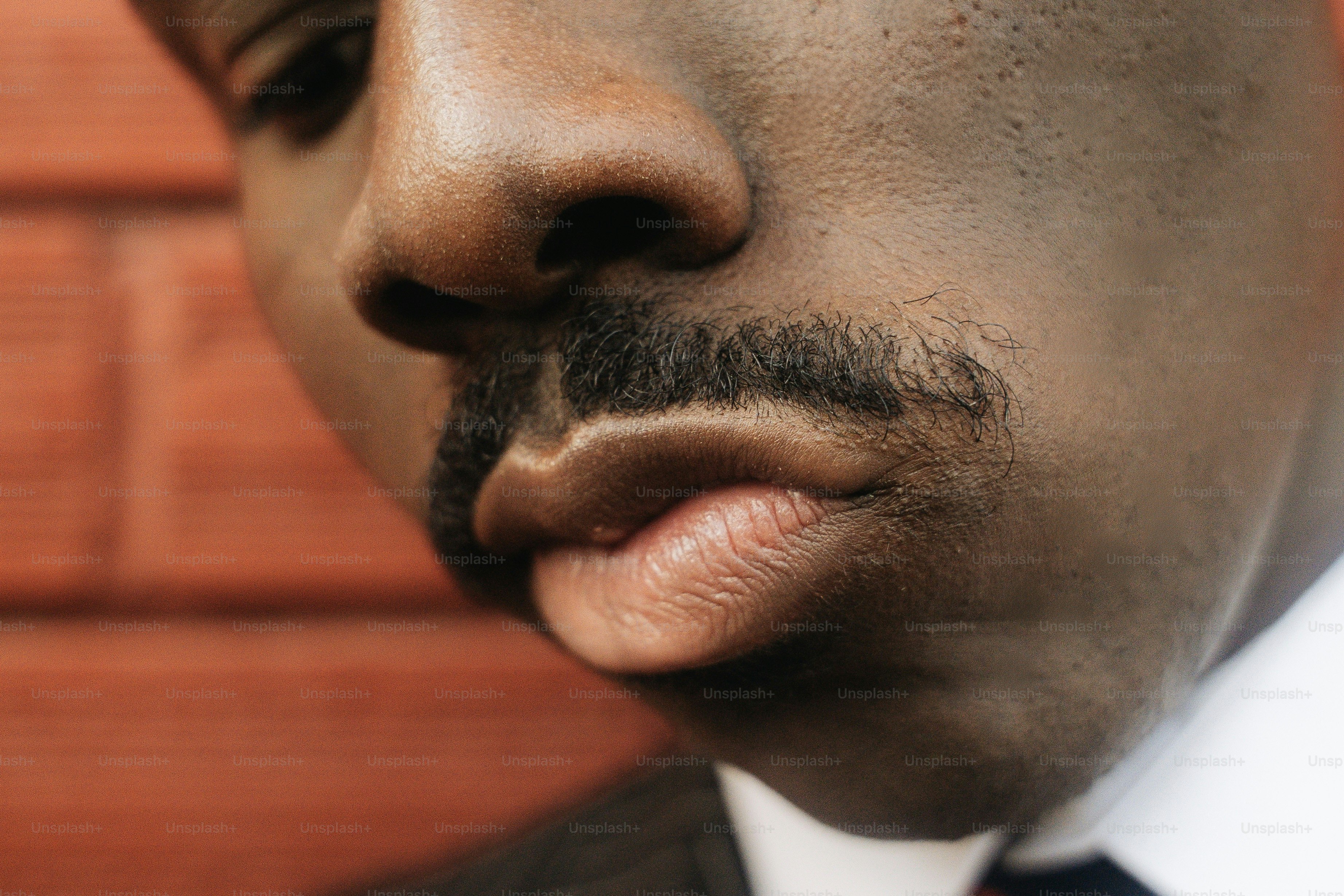 A close-up of a man with a mustache against a red brick wall