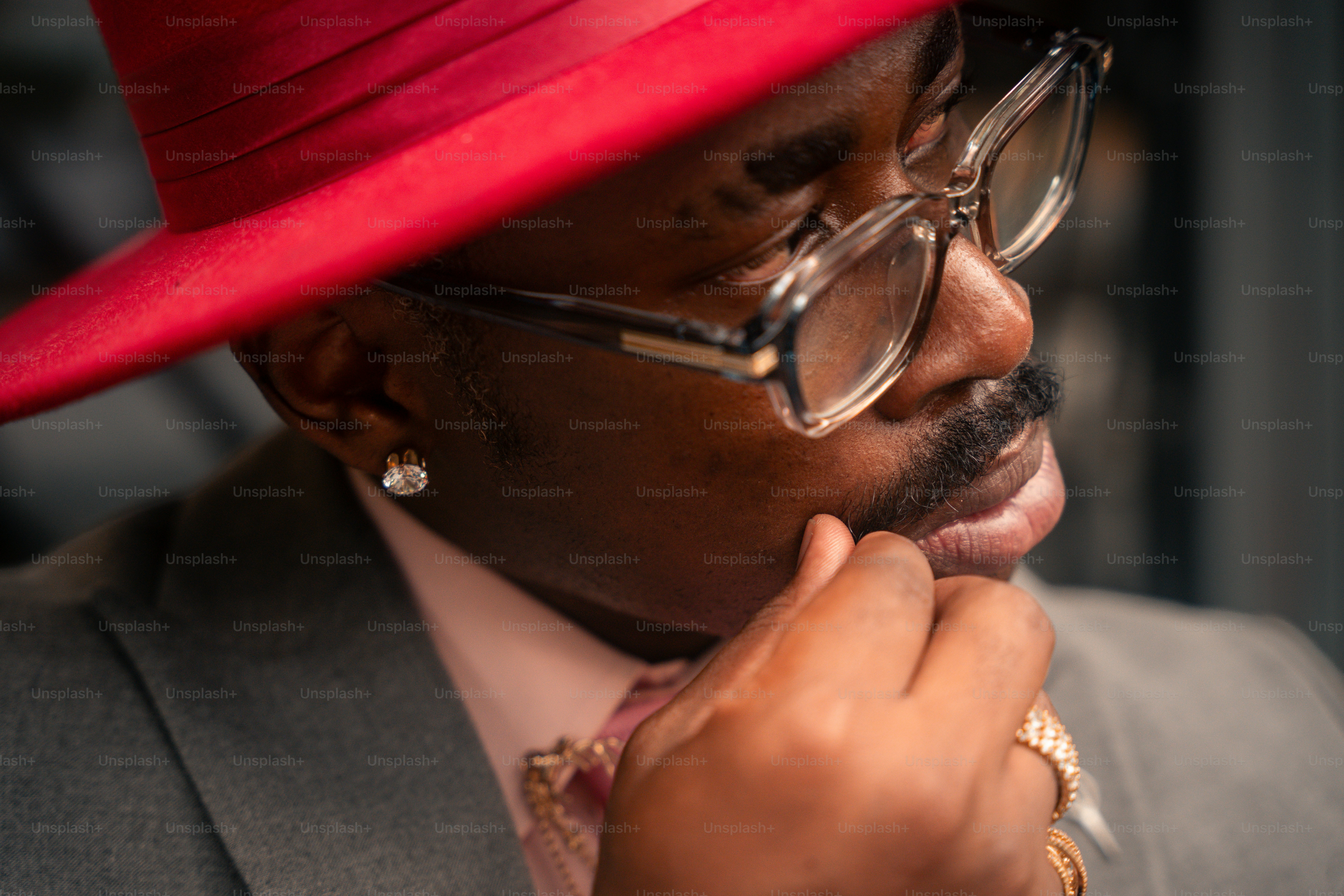 A man in a red fedora and glasses with a hand to his chin