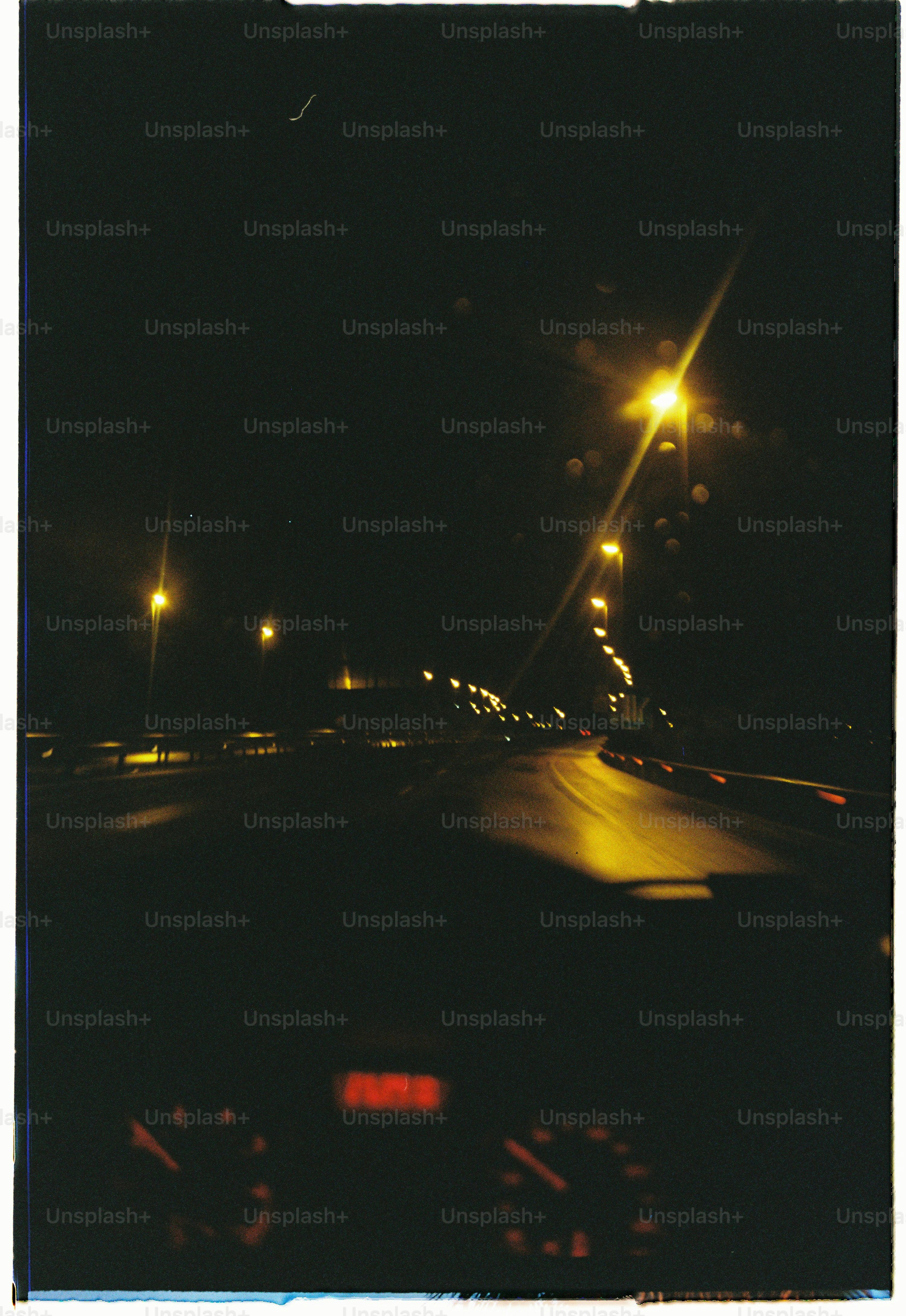 Ein Blick aus dem Armaturenbrett eines Autos auf eine dunkle Autobahn, die nachts von gelben Straßenlaternen erleuchtet wird
