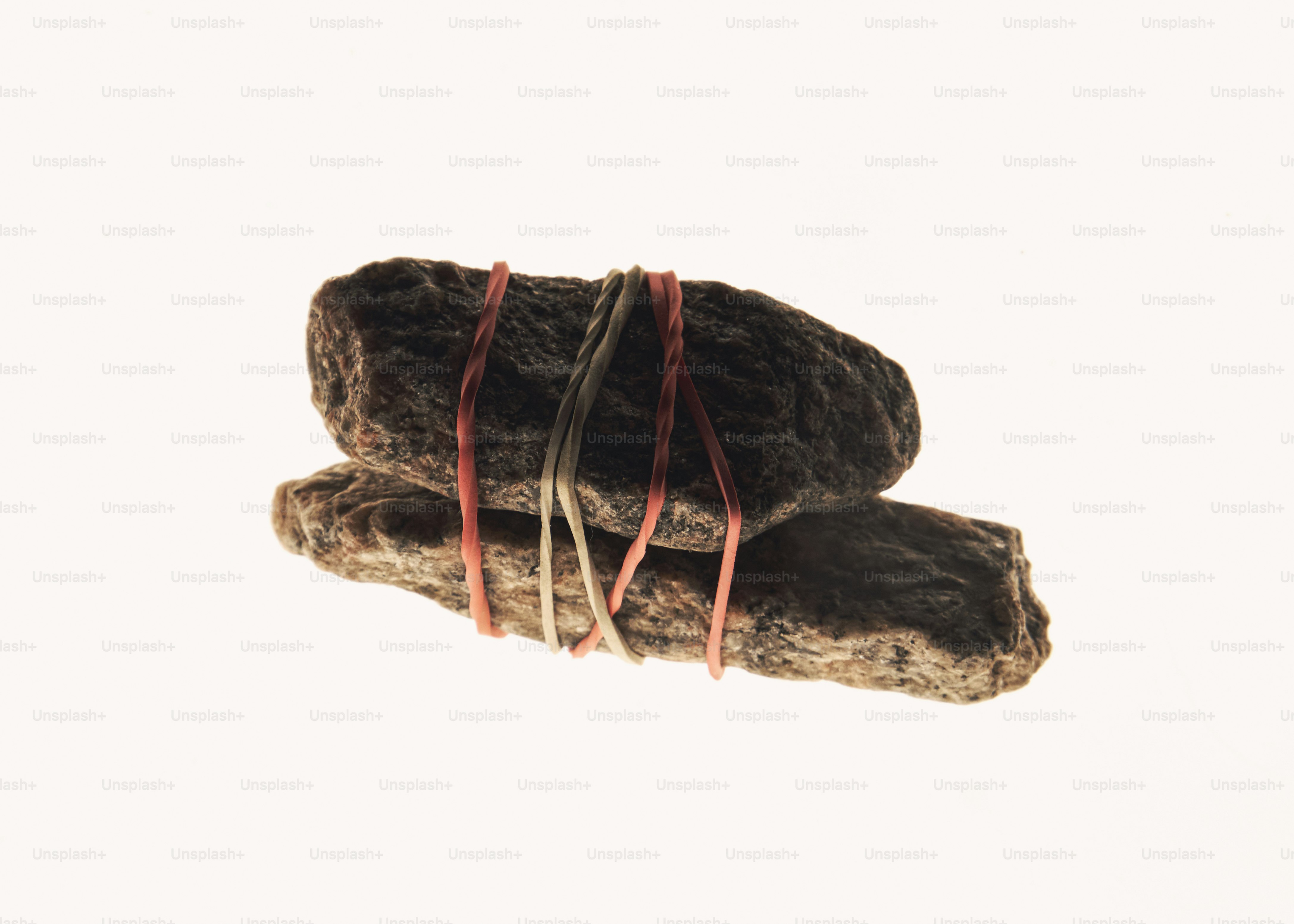 Two rough stones bound together with three thin rubber bands against a white background
