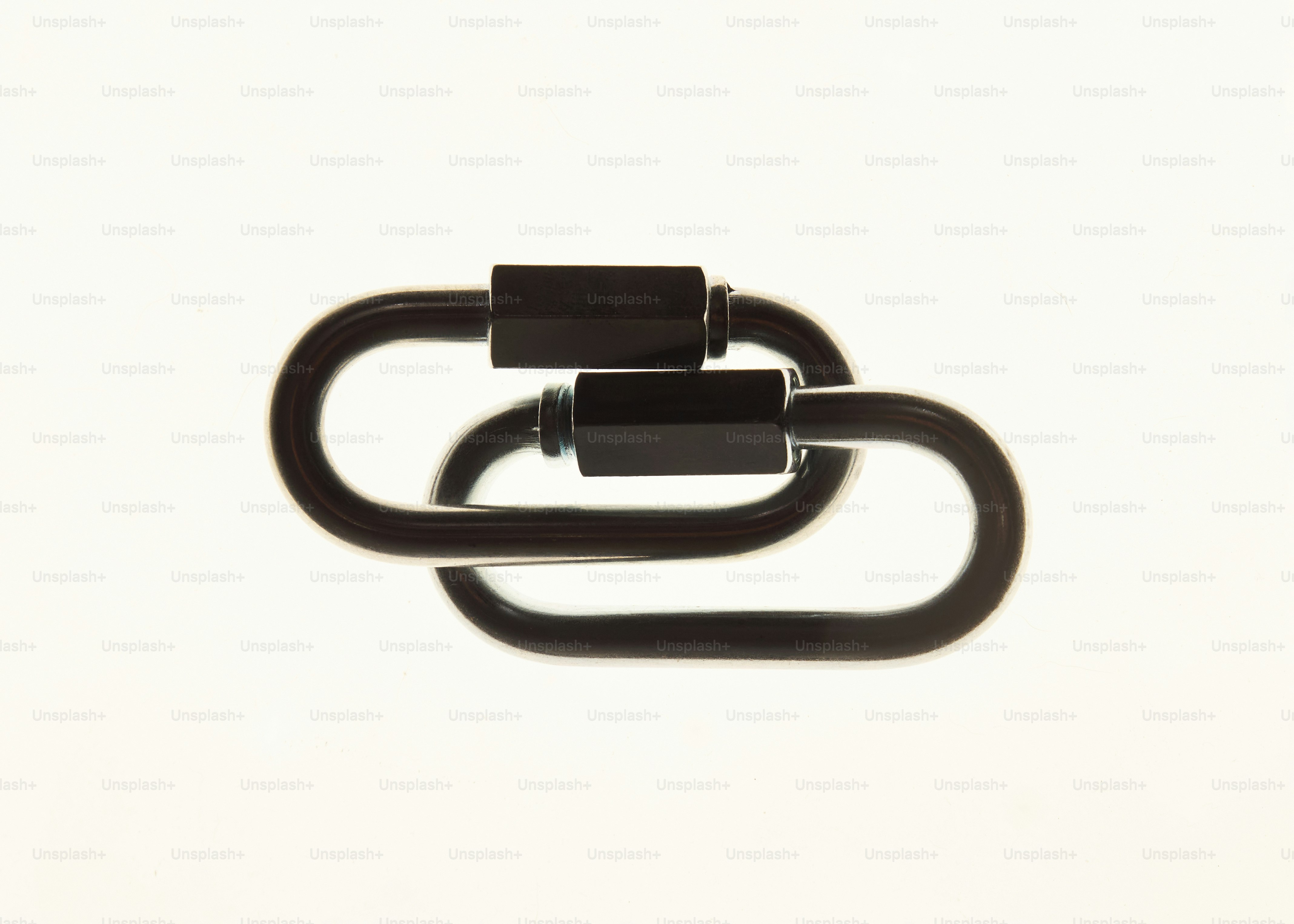 Two black metal carabiners linked together against a bright white background