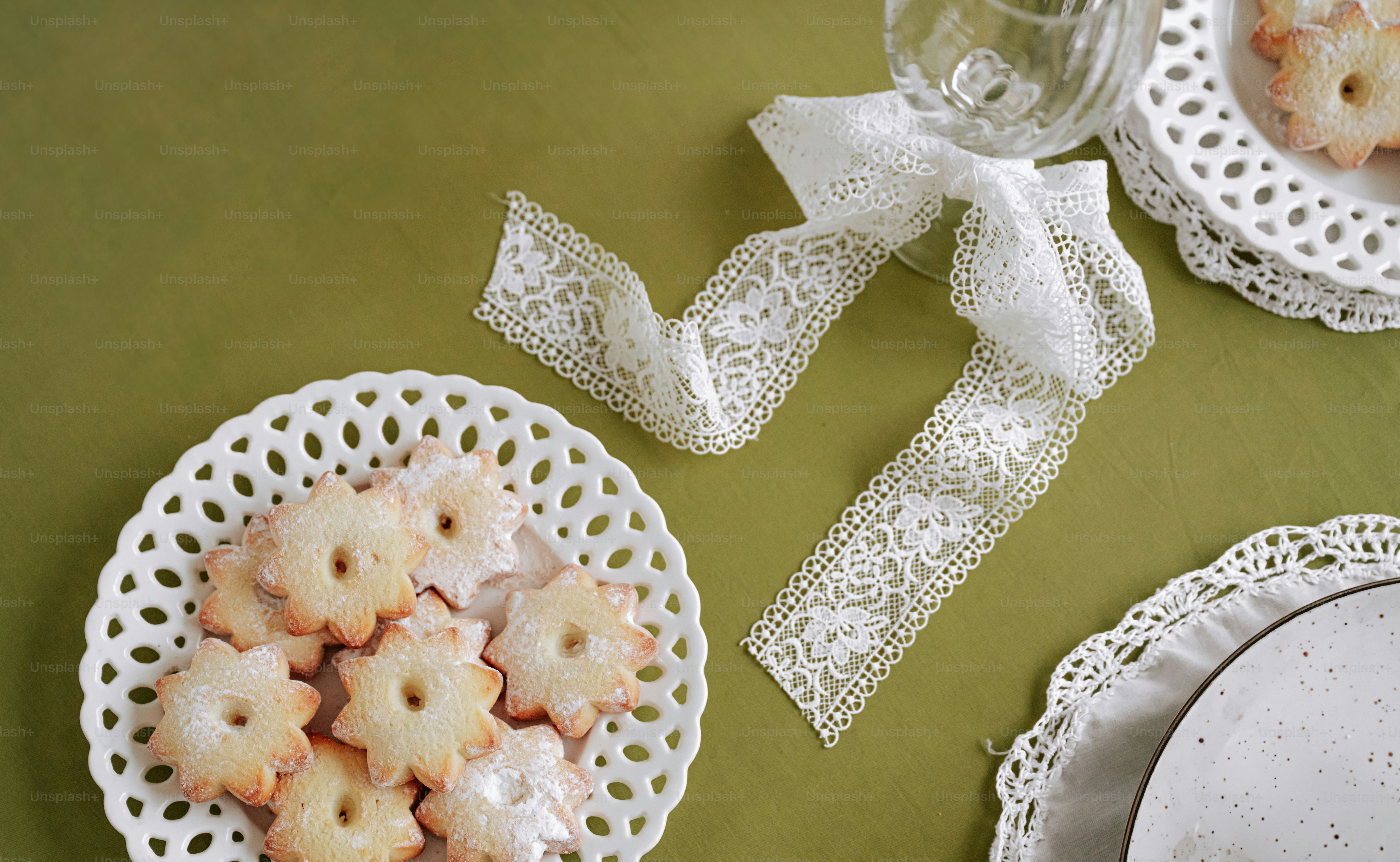 Star-shaped cookies on a white lattice plate beside a white lace ribbon on a green tablecloth