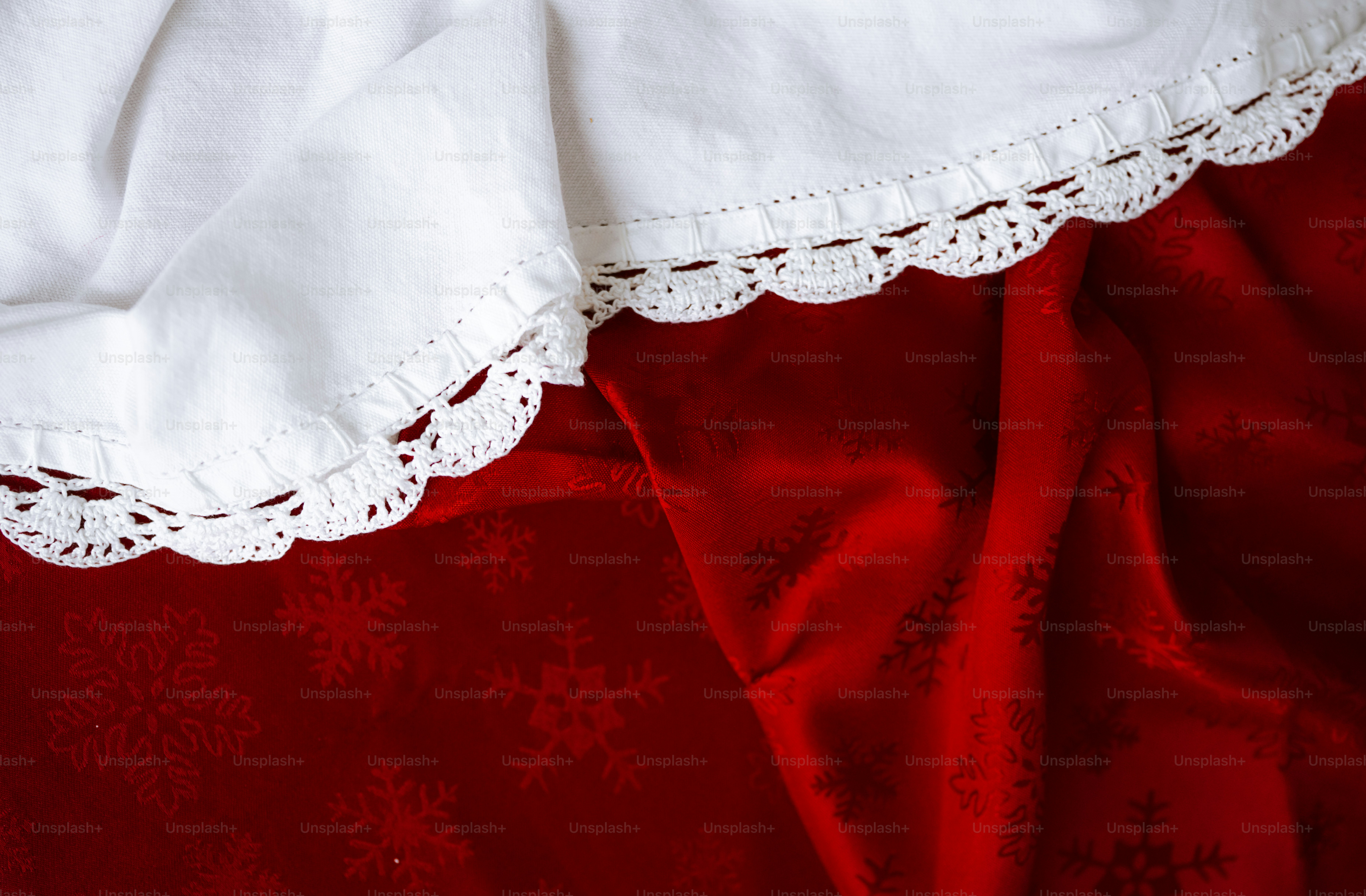 A white fabric with a crocheted lace edge draped over a red cloth with snowflake patterns