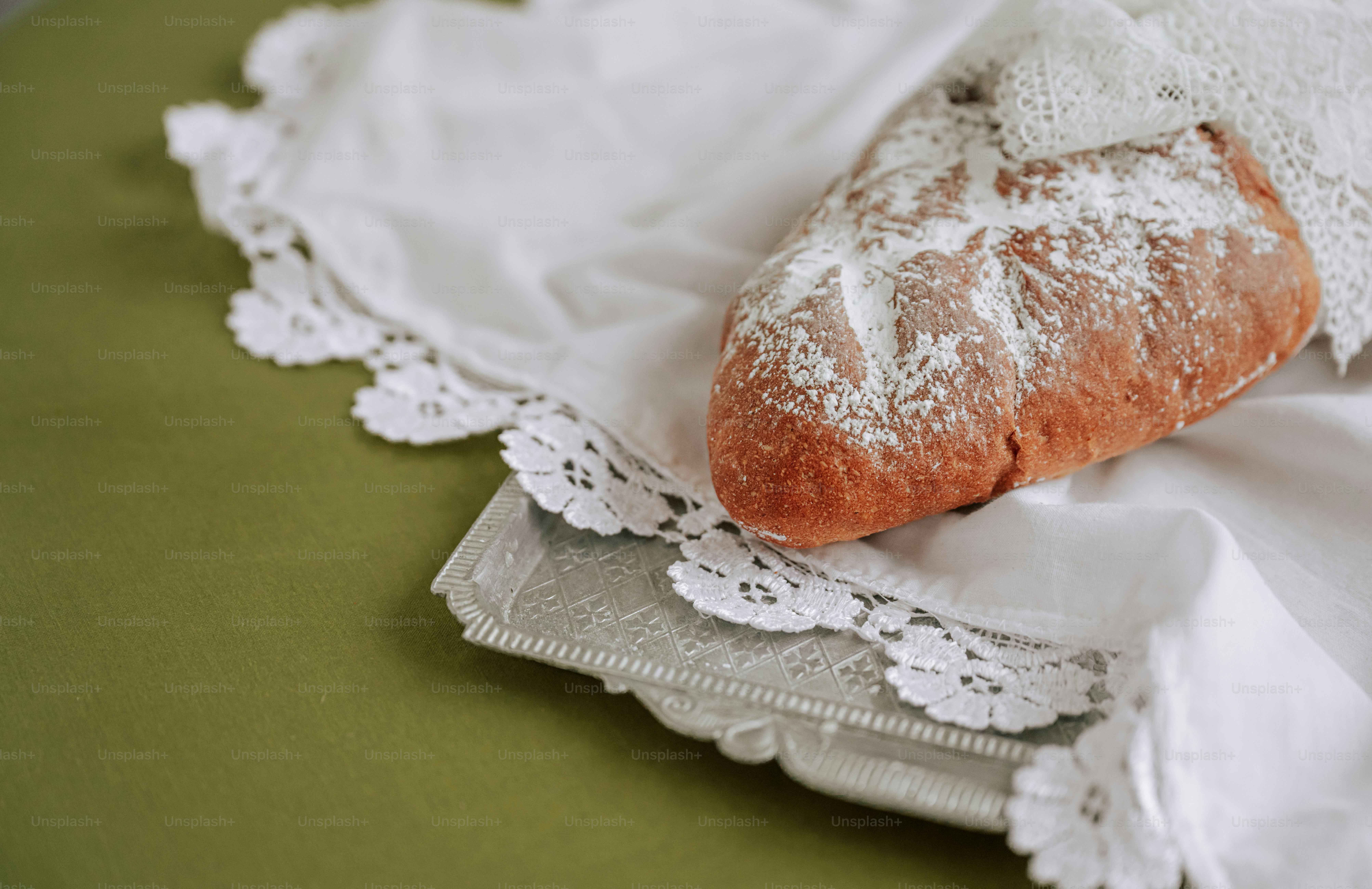 A loaf of crusty bread dusted with flour on a white lace cloth