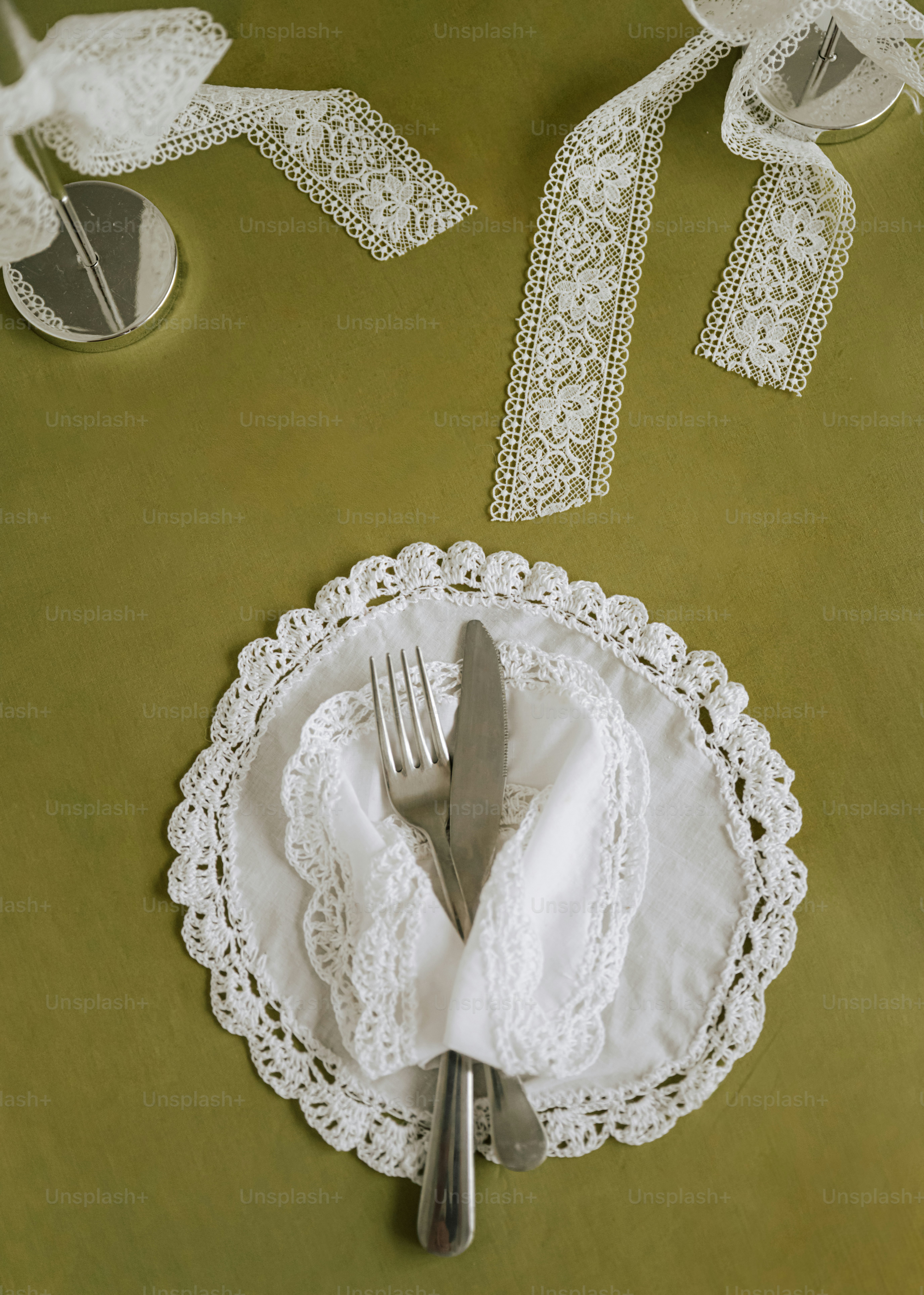 A fork and knife wrapped in a white lace napkin on a green tablecloth