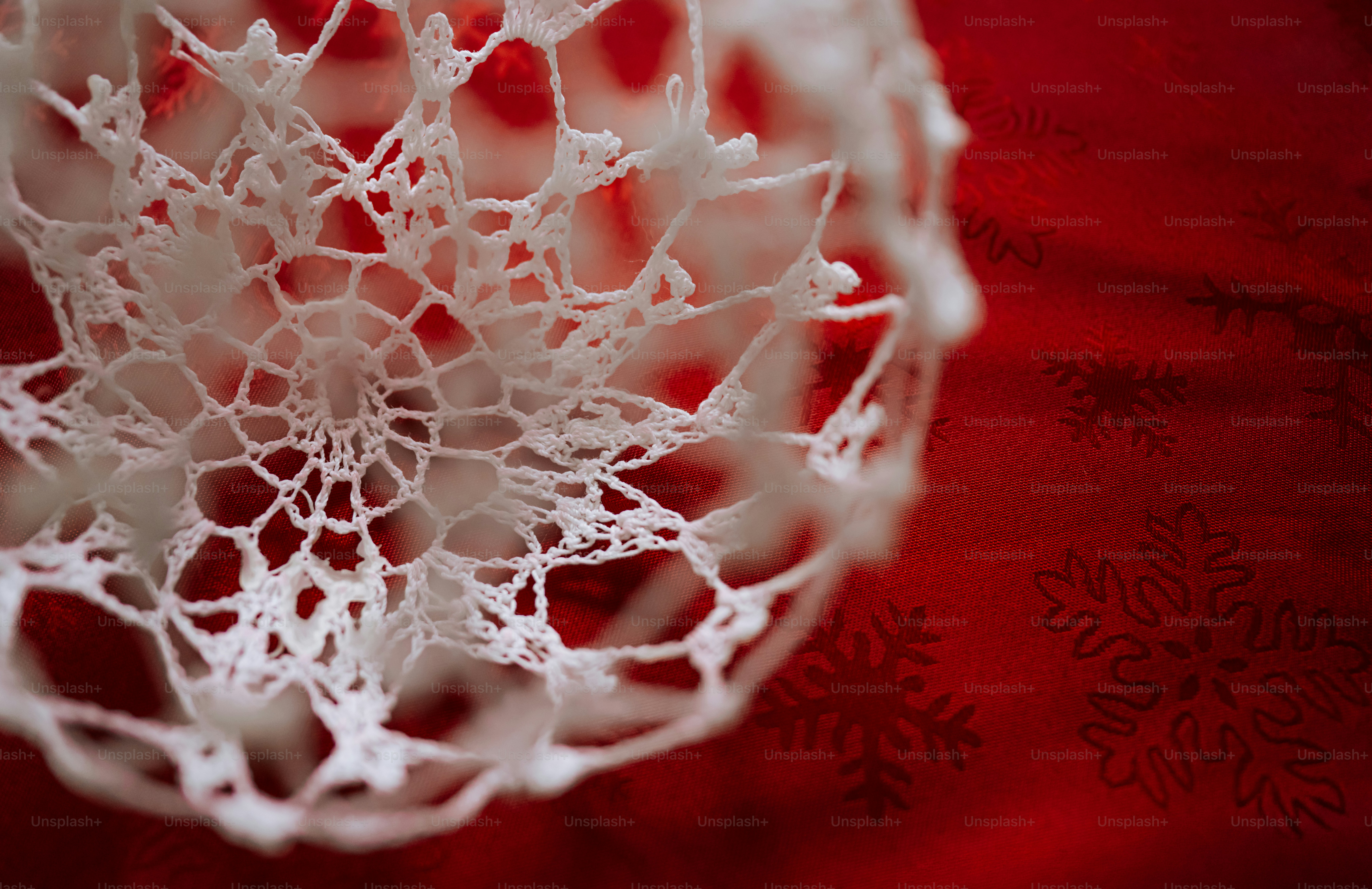A white crocheted ornament with a delicate lace pattern against a red fabric with snowflake prints