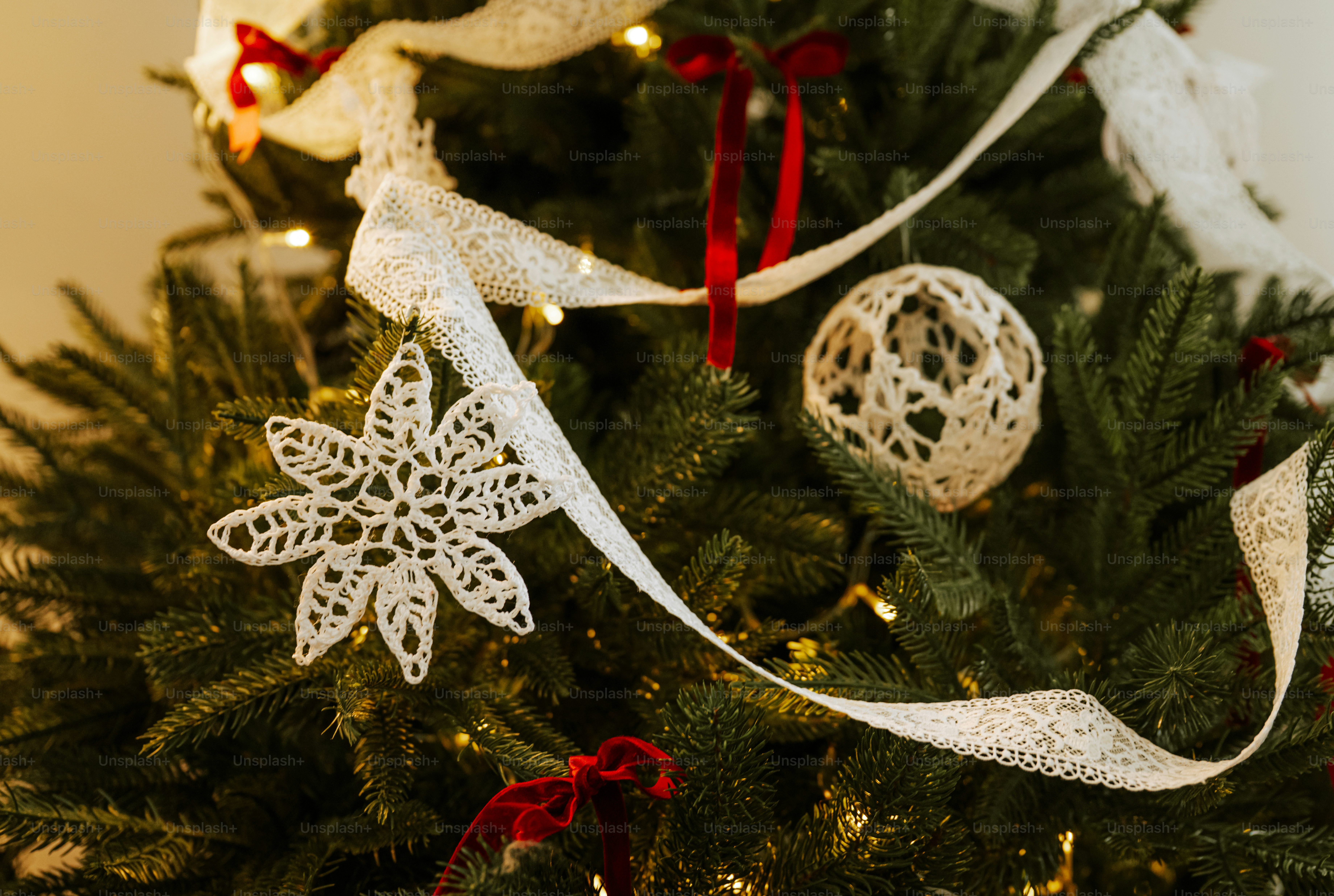 A Christmas tree decorated with white lace ornaments, ribbons, and small red bows