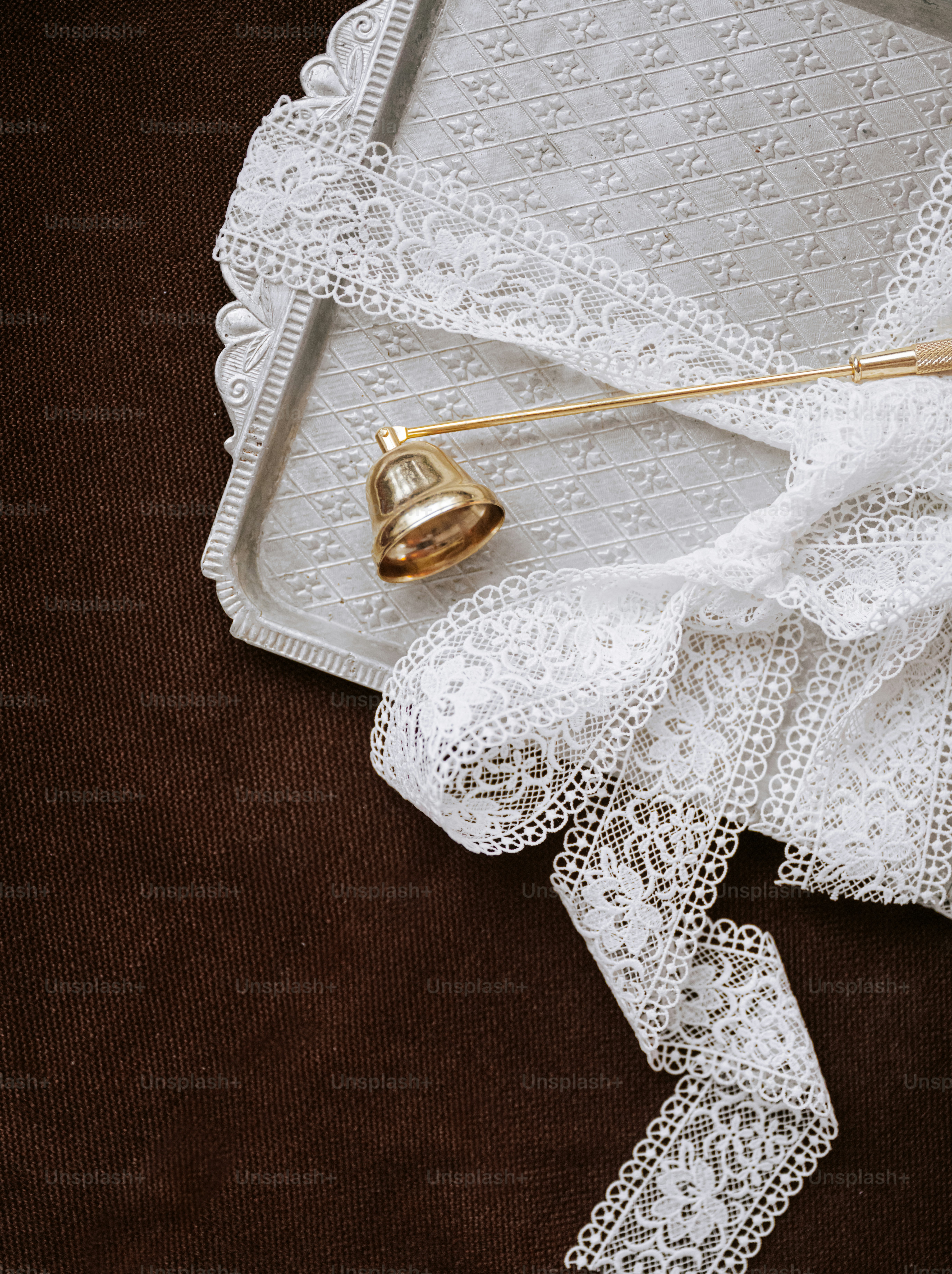 A gold candle snuffer bell and white lace ribbon on a decorative silver tray
