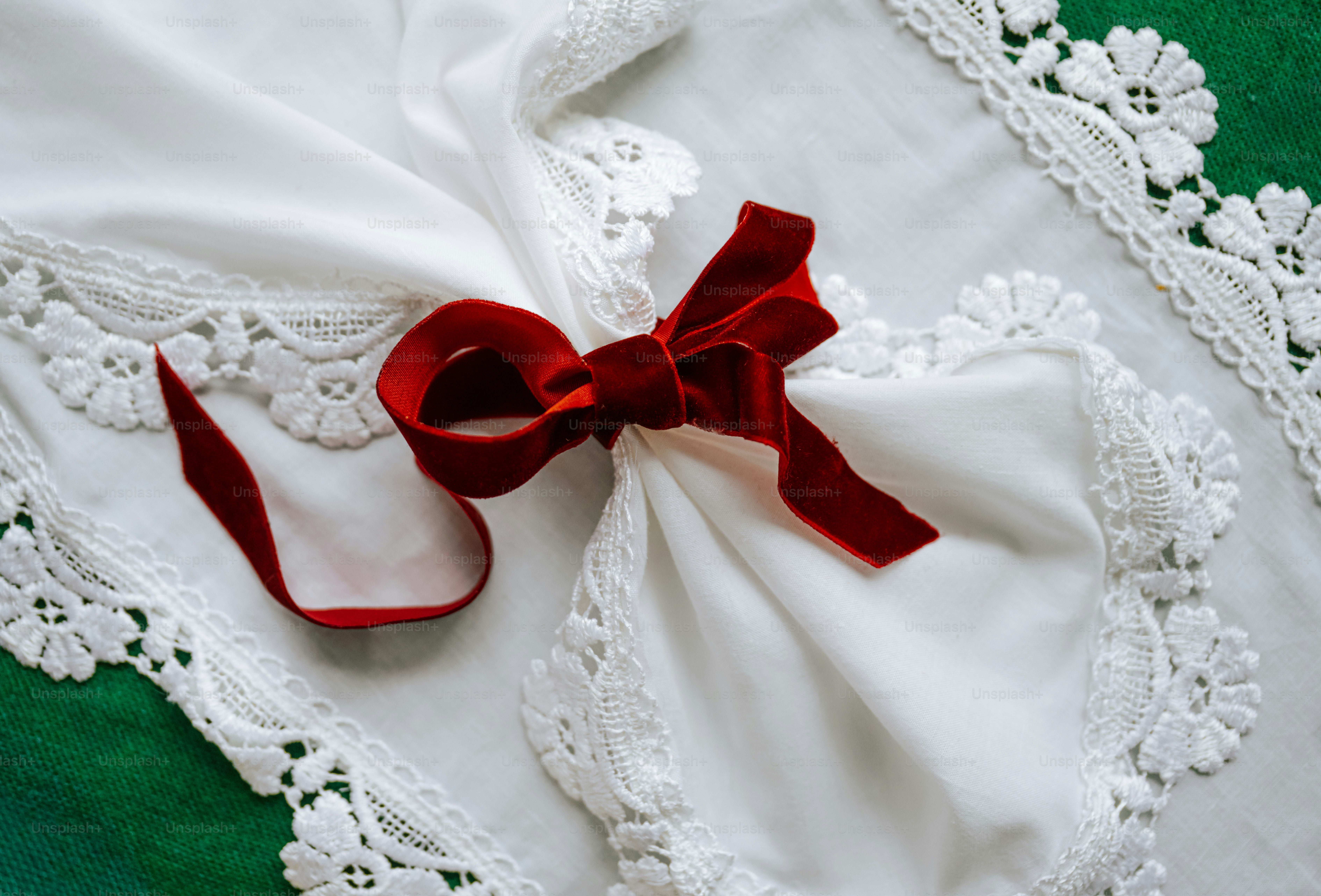 A red velvet ribbon tied around a white lace-trimmed cloth on a green surface