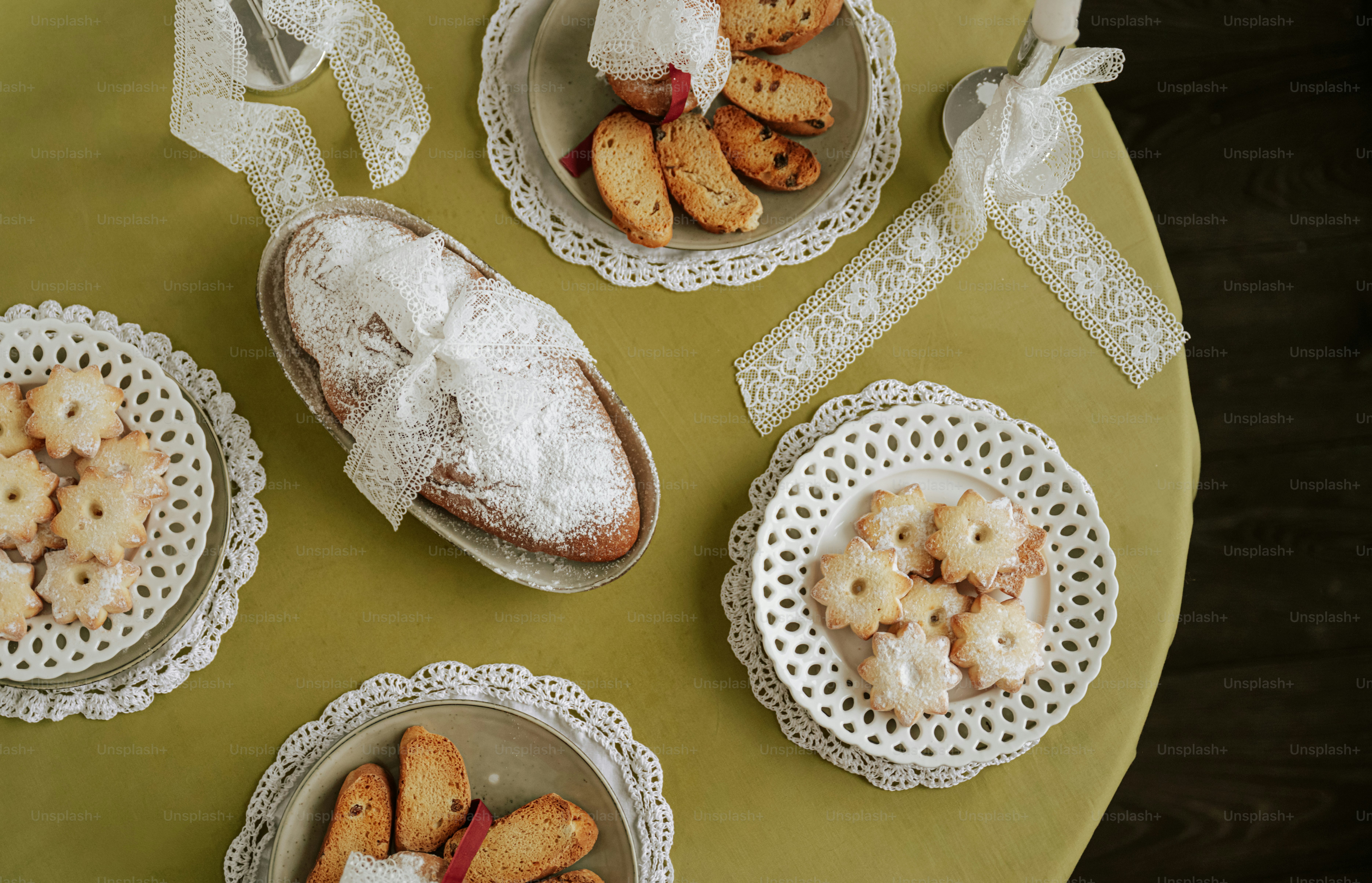 A loaf of bread and star-shaped cookies on plates with lace doilies on a green tablecloth