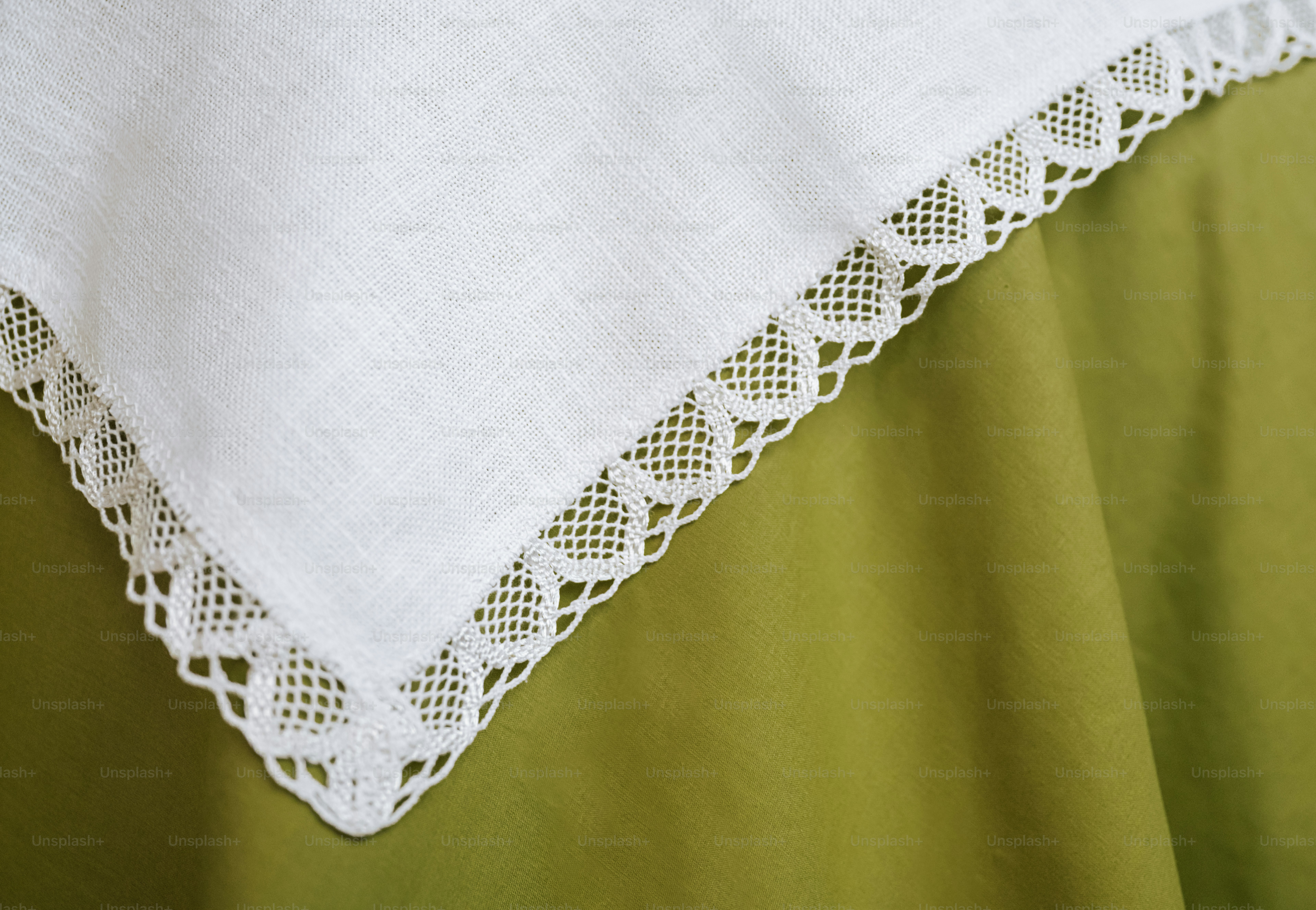 A white linen cloth with a delicate lace border draped over a green fabric