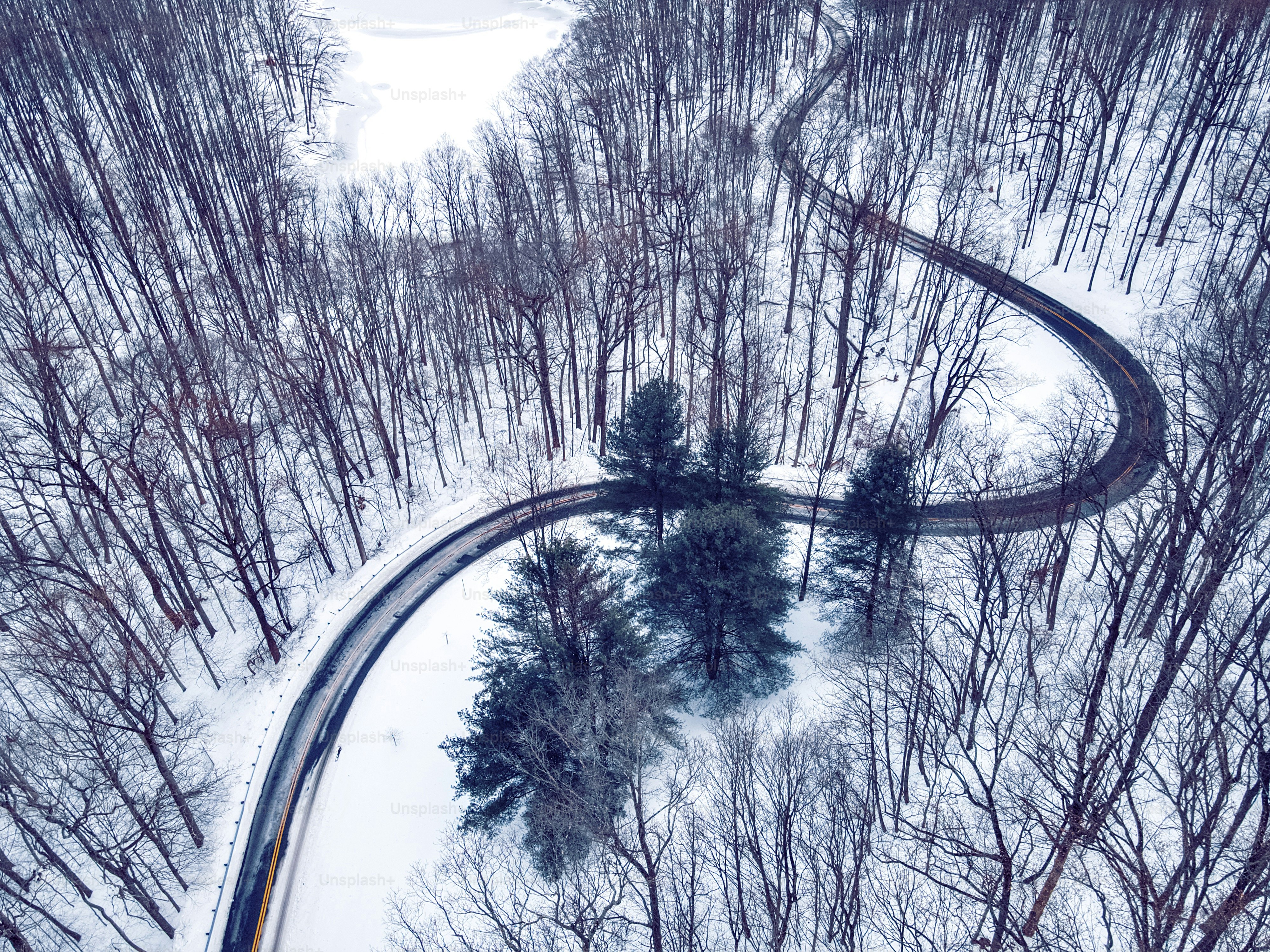 An aerial view of a winding road cutting through a snow-covered forest with bare trees