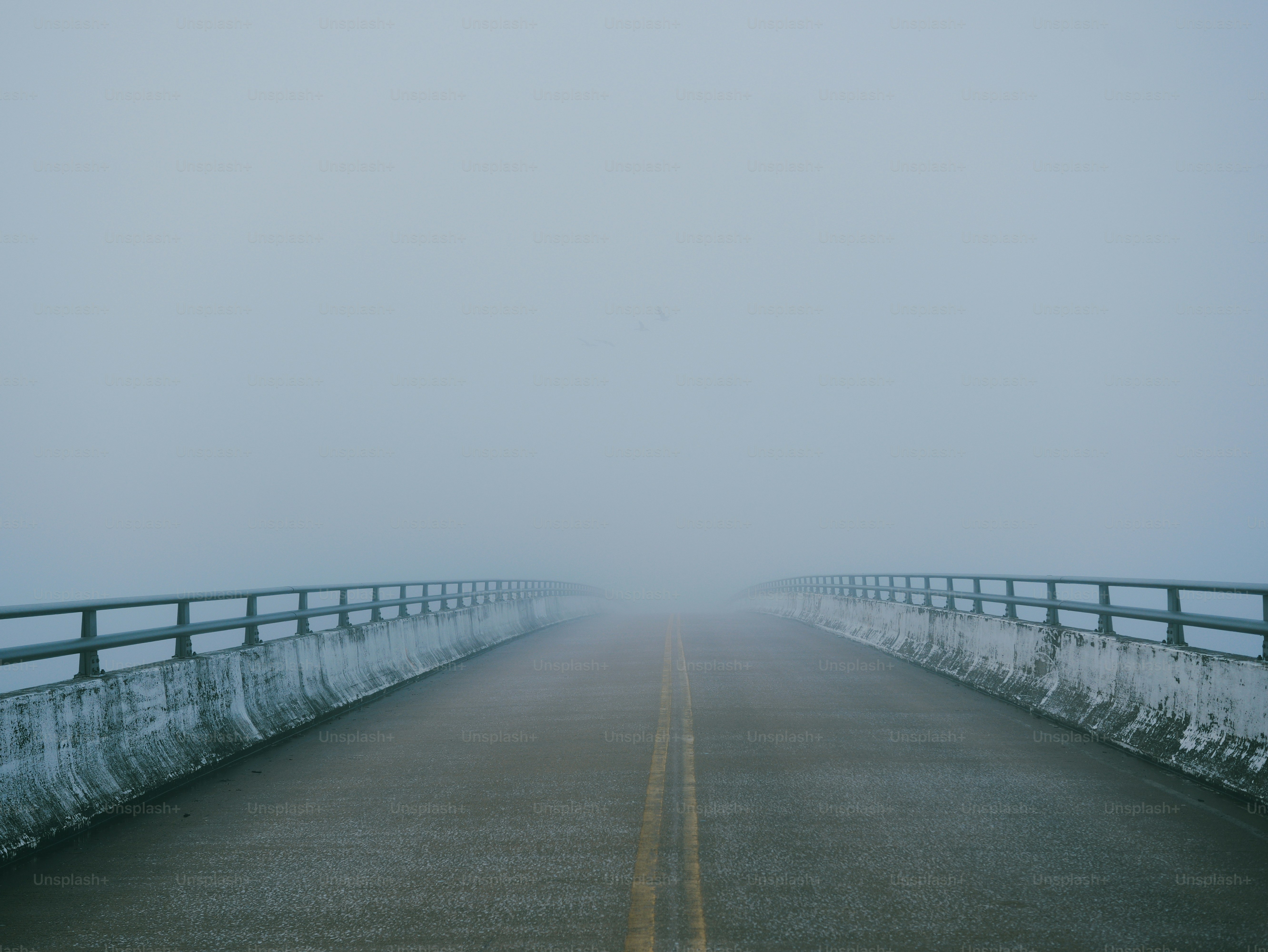 An empty bridge with concrete barriers and metal railings disappearing into thick grey fog