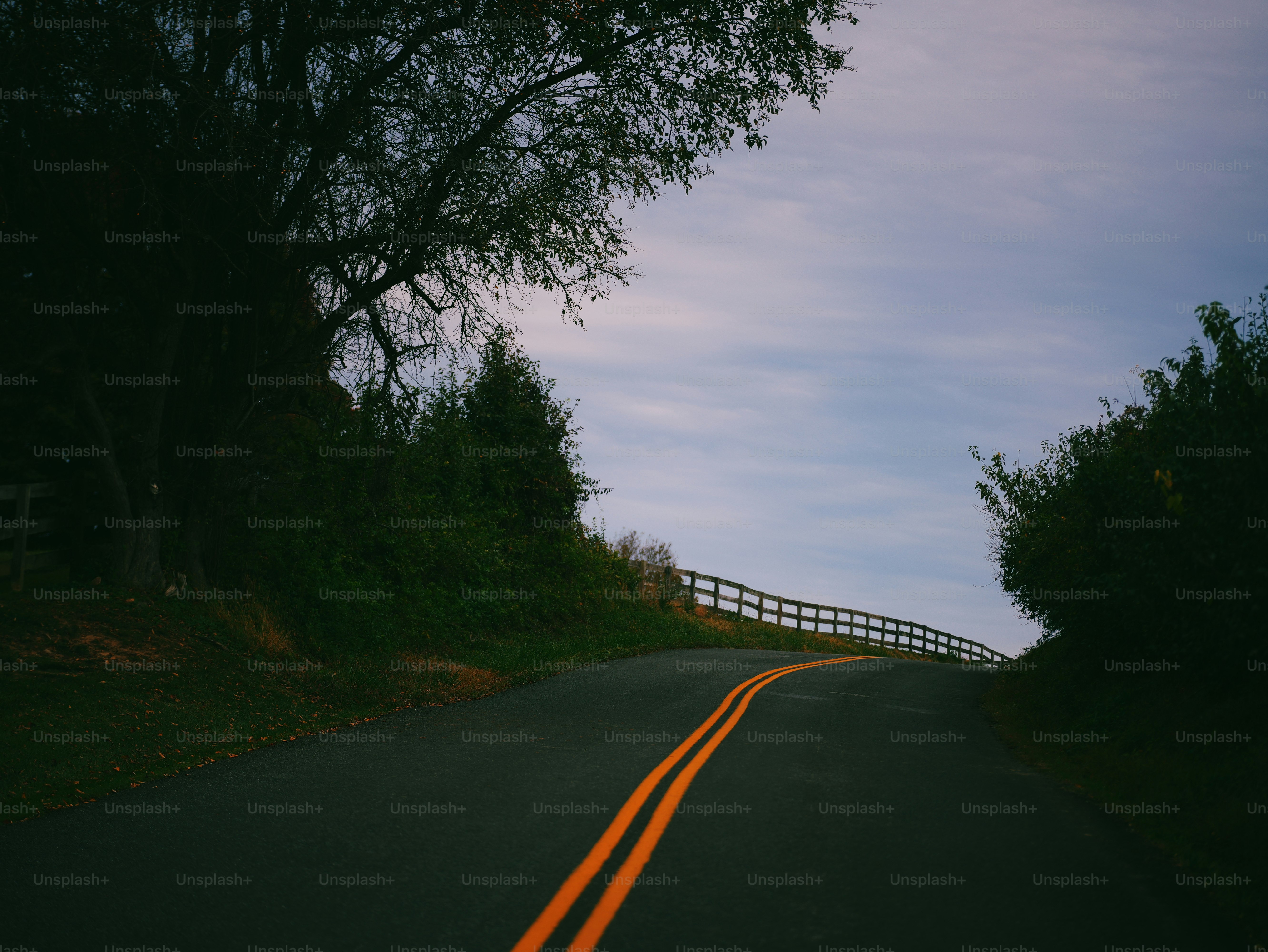 A winding country road with yellow centerlines climbing toward a hill under an overcast sky