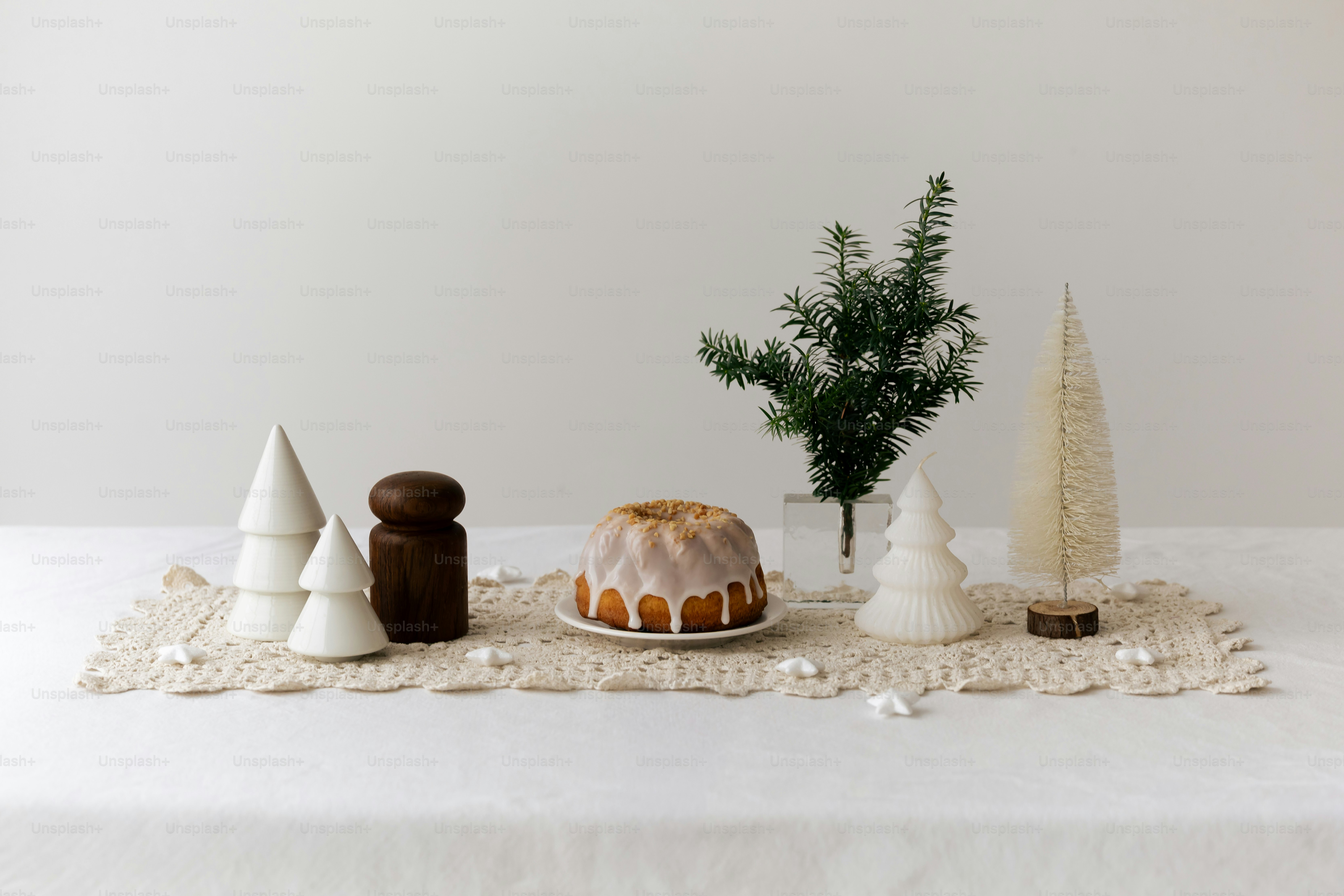 A small bundt cake with white icing on a lace runner with decorative trees and greenery