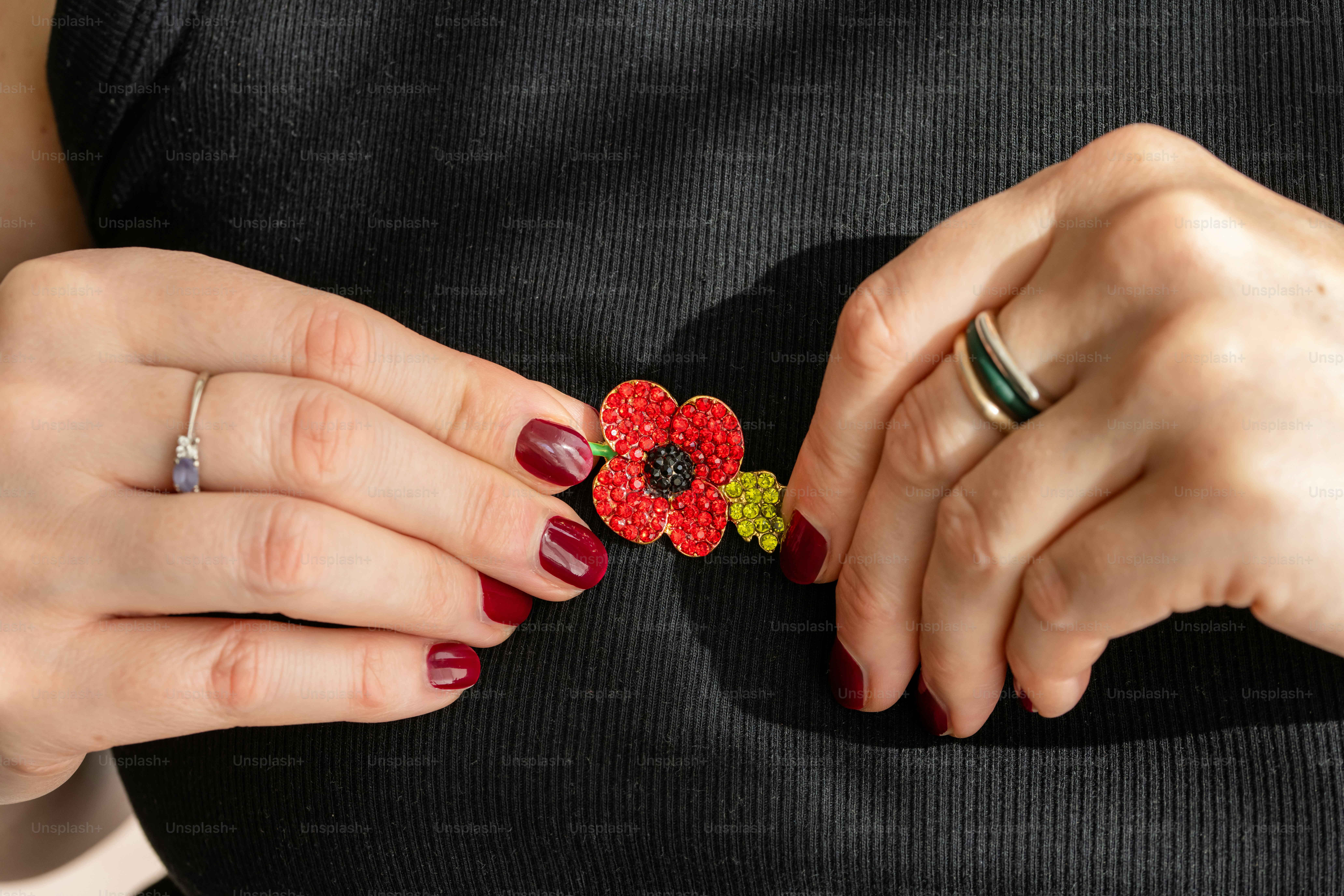 A person pinning a red poppy brooch with sparkling crystals onto a black shirt