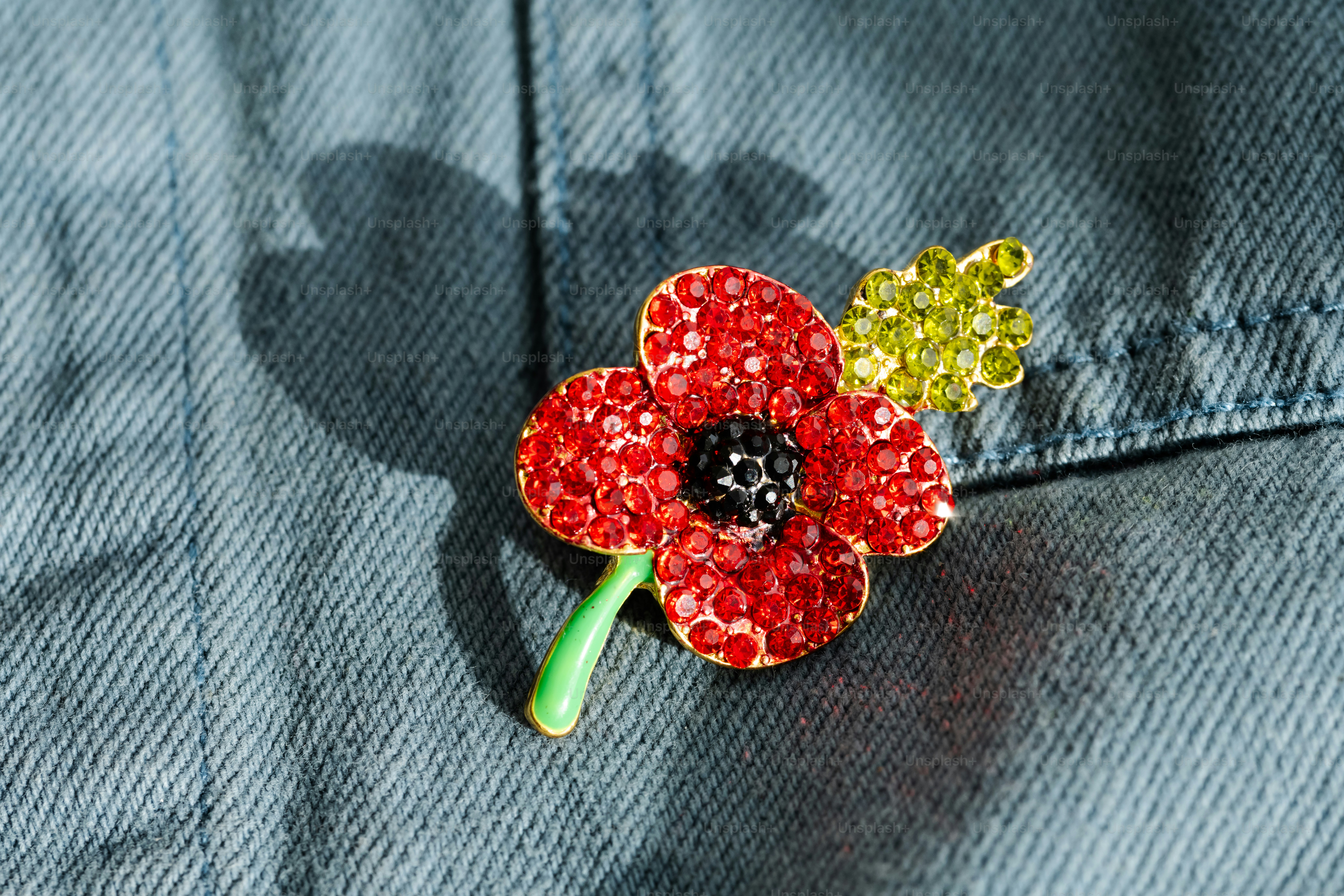 A red poppy brooch with green crystal leaves pinned to blue denim fabric