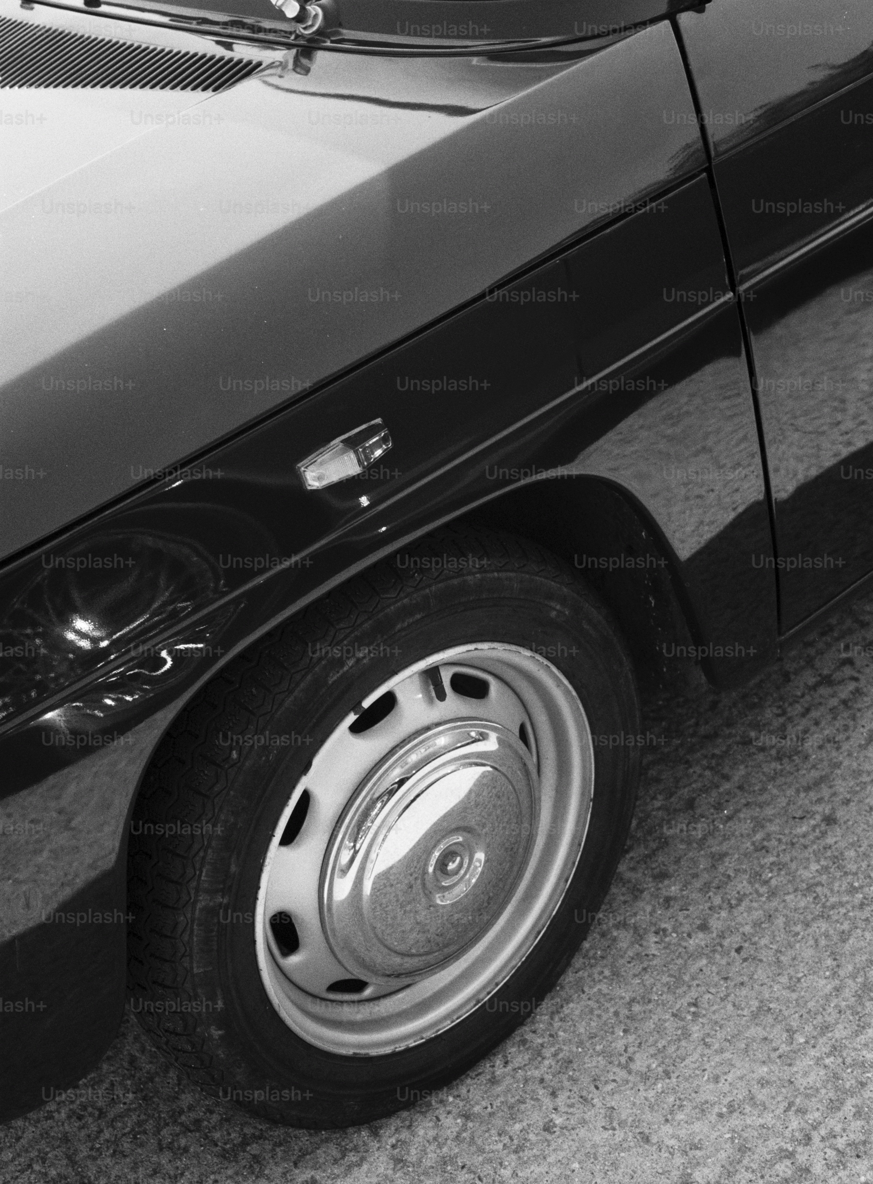 A black and white close-up of a car wheel and fender on asphalt
