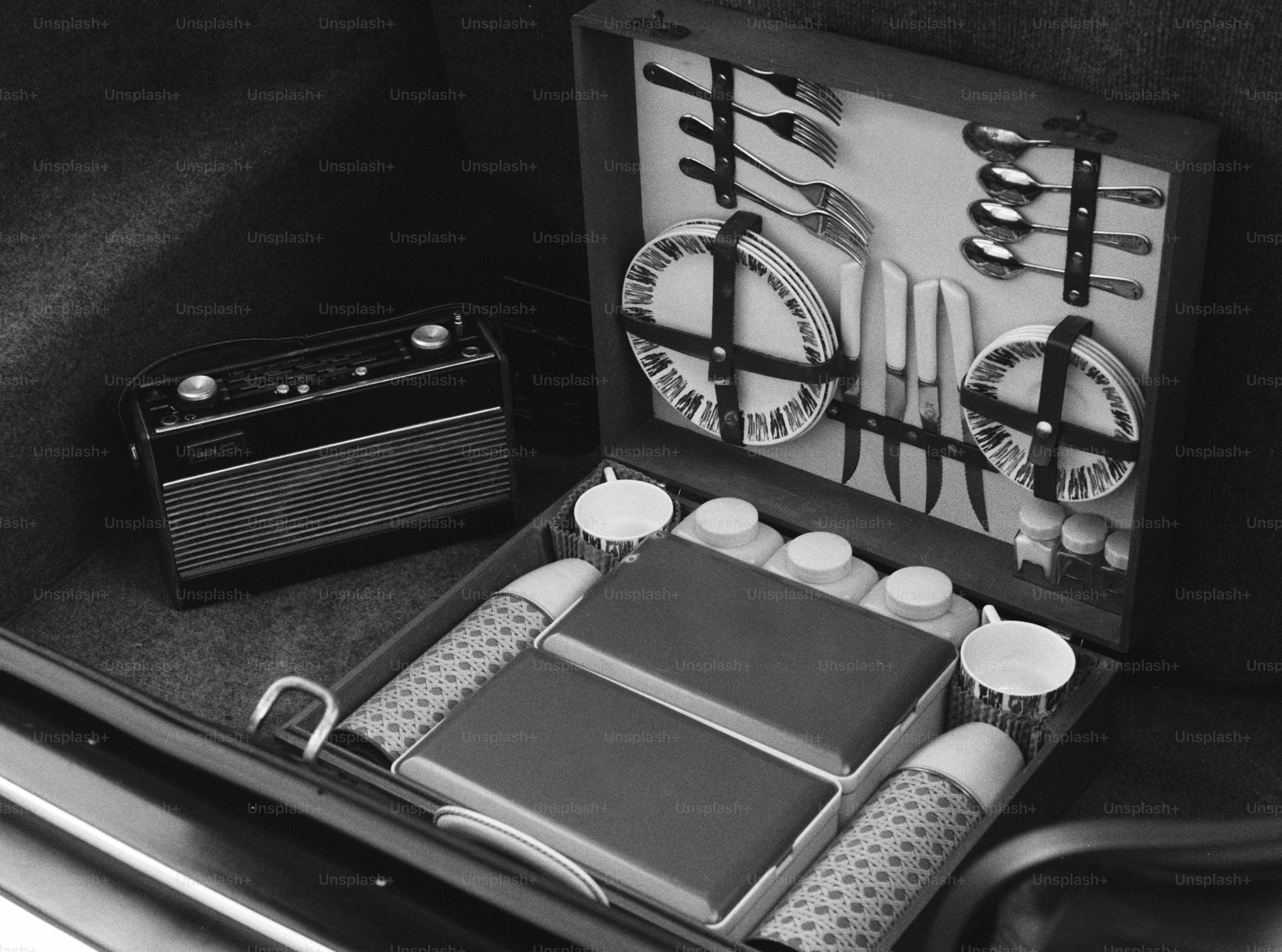 A black and white picnic set in a case beside a vintage radio