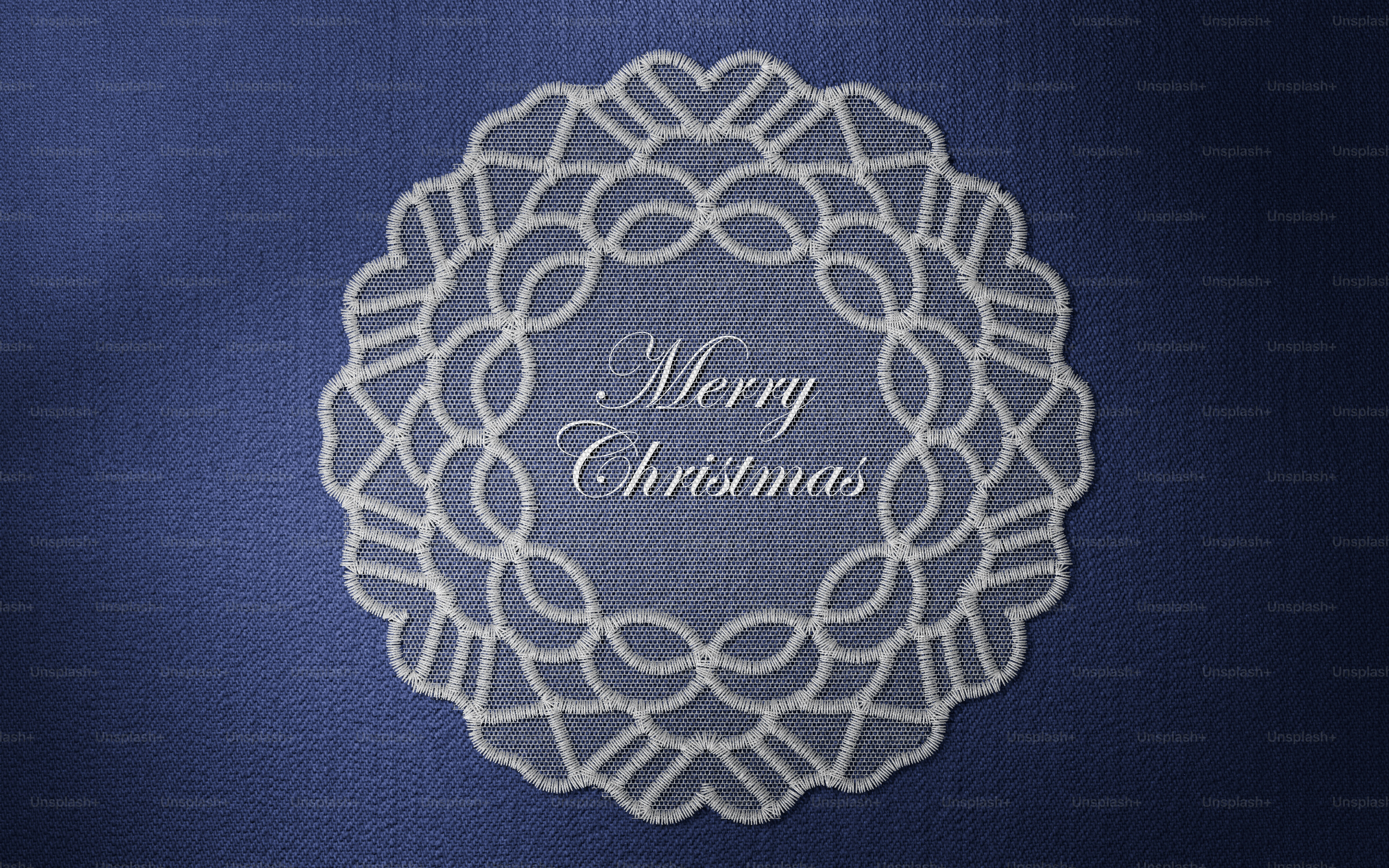 A white lace doily with the text Merry Christmas on a dark blue denim background