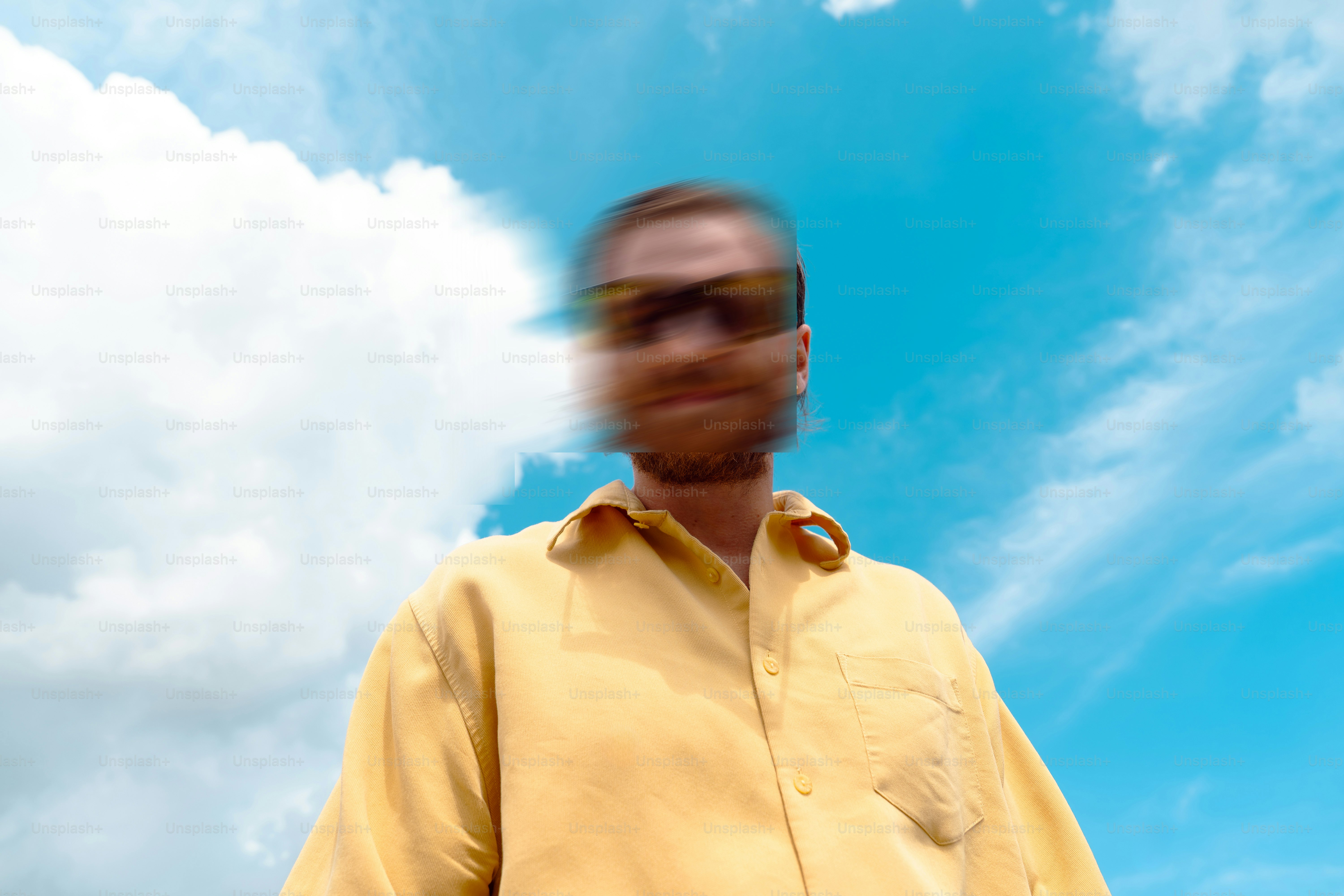 A person in a yellow shirt with a motion-blurred face against a bright blue sky