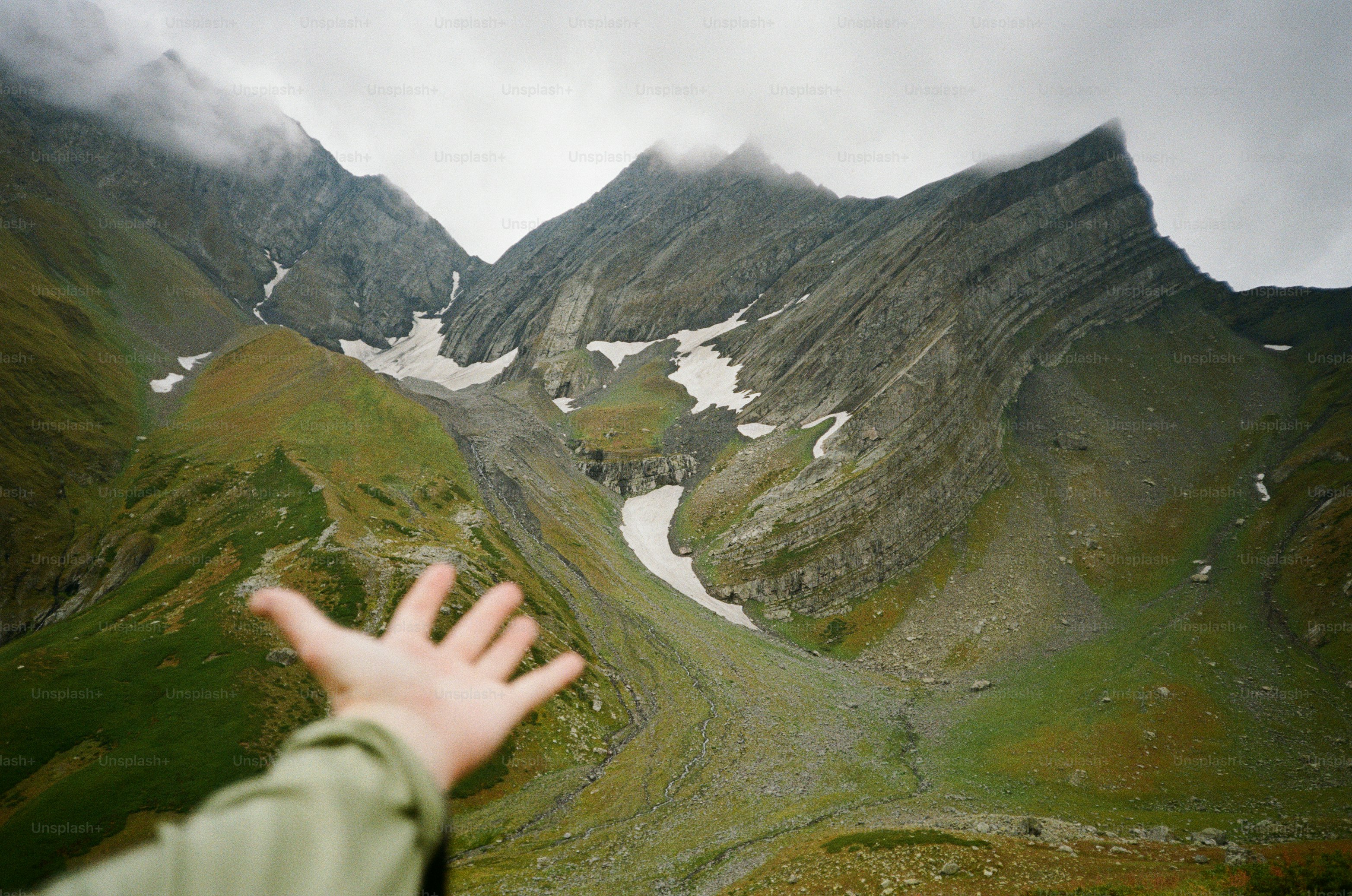 Hand reaching toward mountain landscape - Photo on Unsplash+