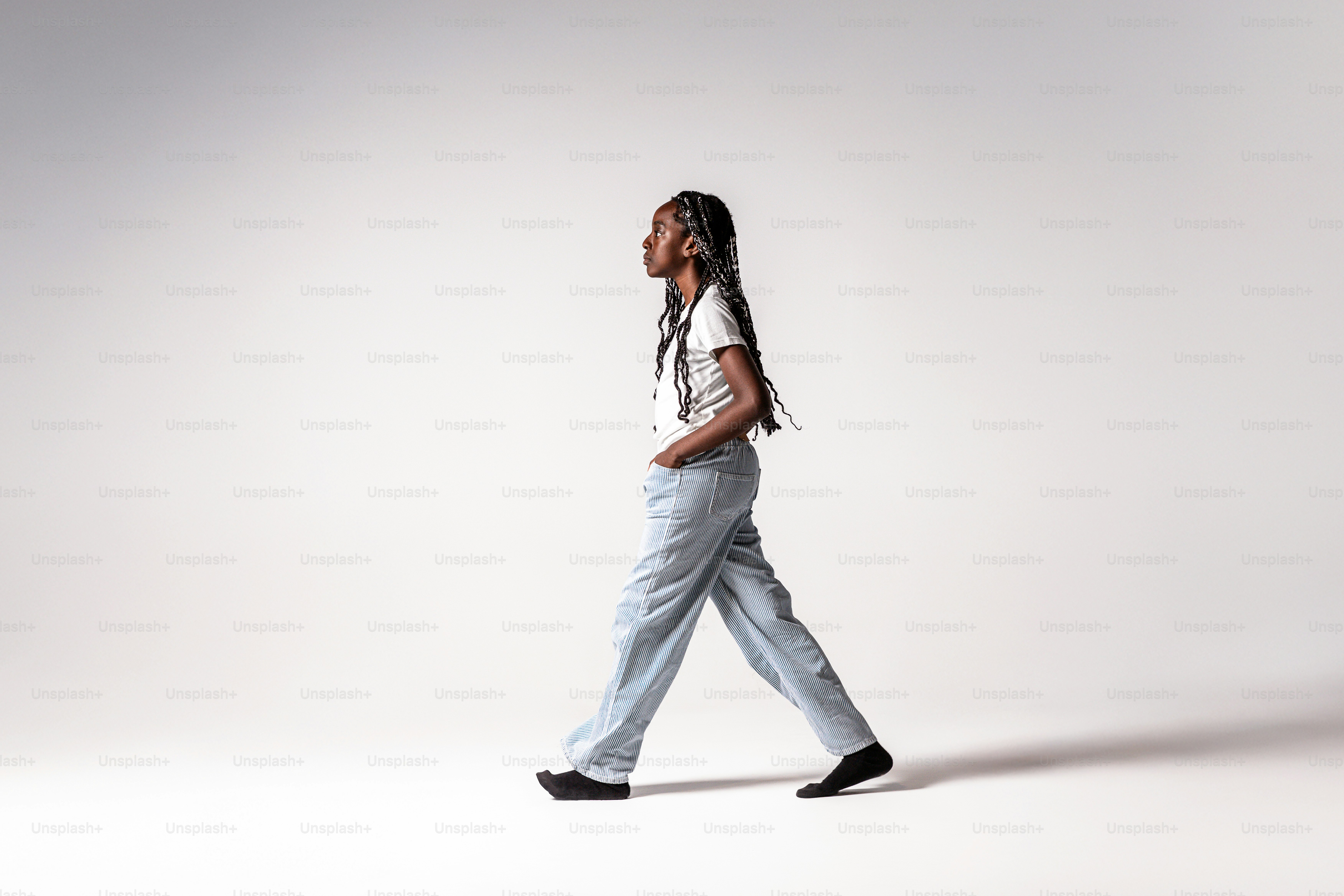 A person with long braided hair walking in a white t-shirt and light blue trousers