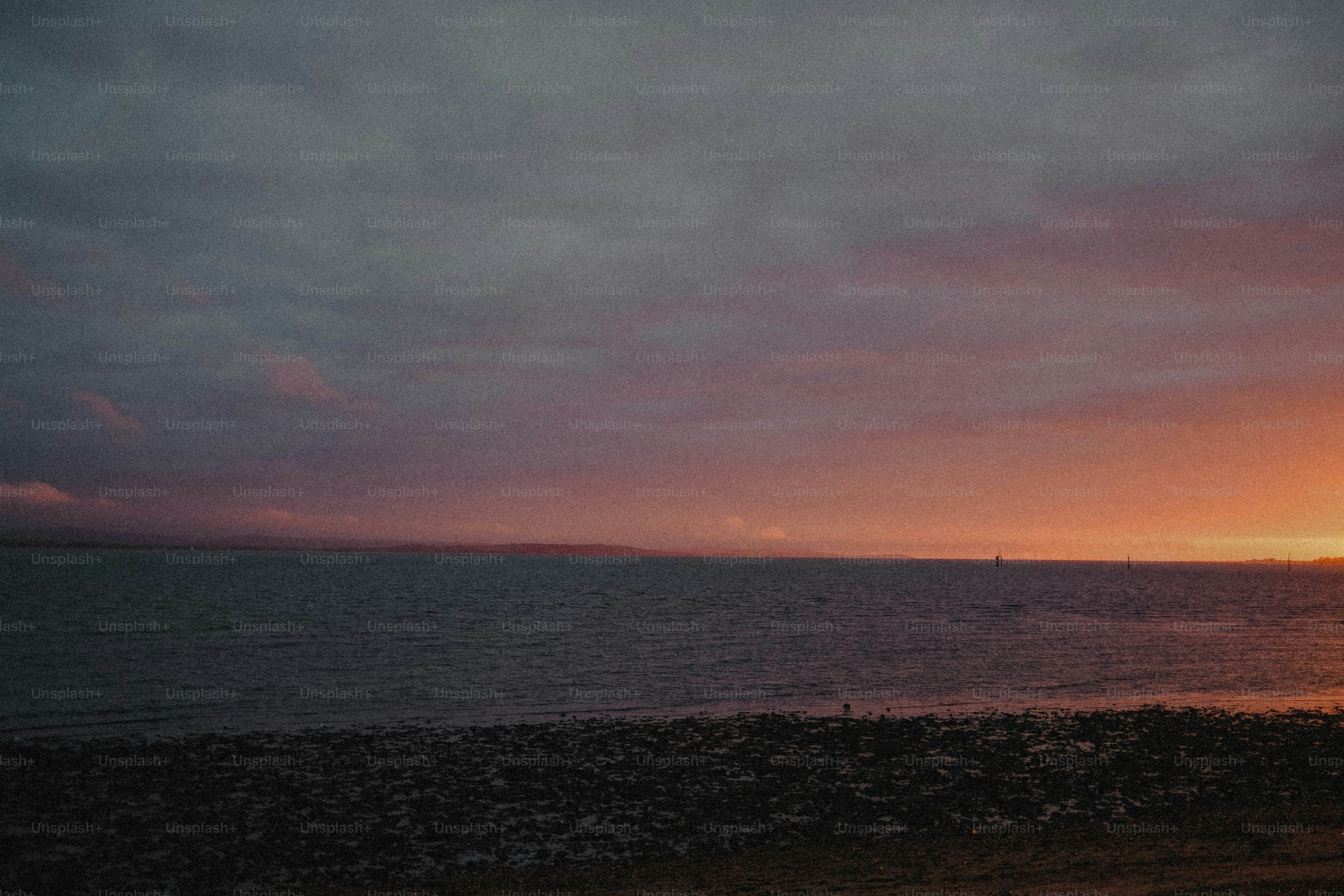 Dark water under a cloudy sky with a warm orange glow on the horizon