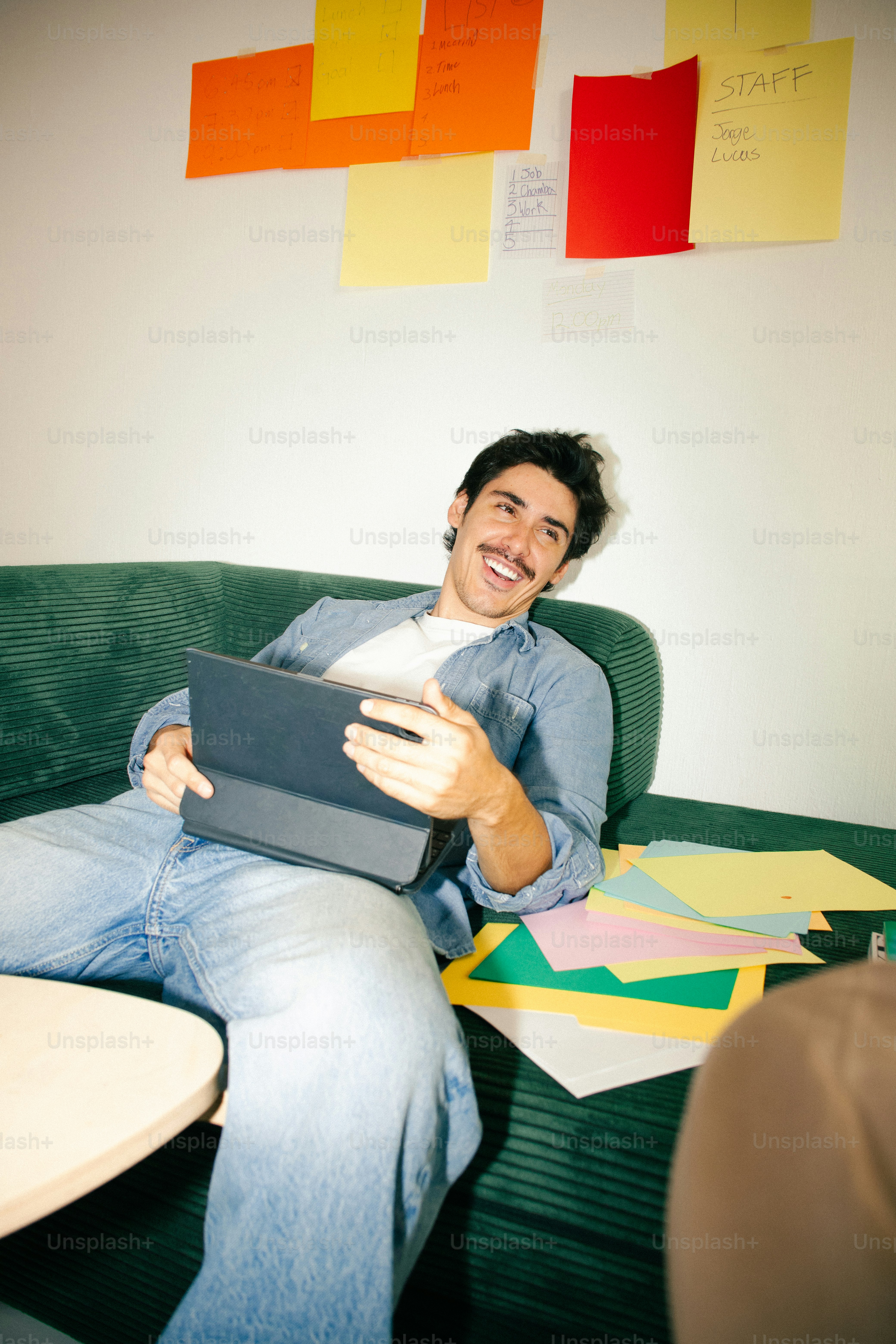 Man laughing with tablet on sofa - Photo on Unsplash+