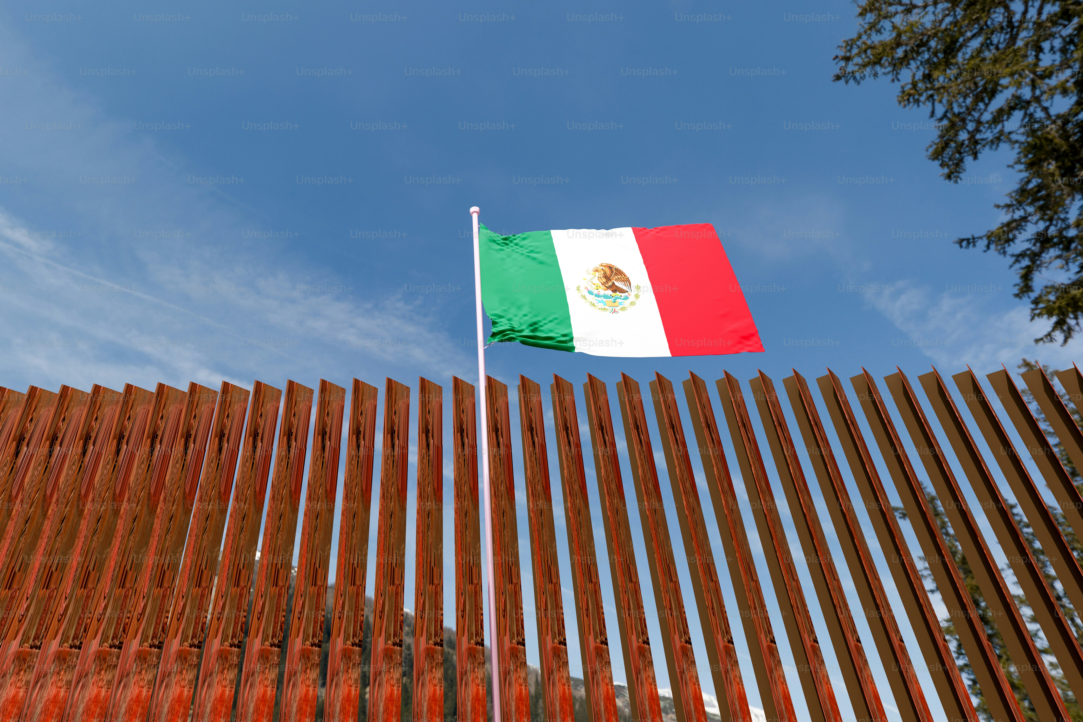 Mexican flag behind metal border fence - Photo on Unsplash+