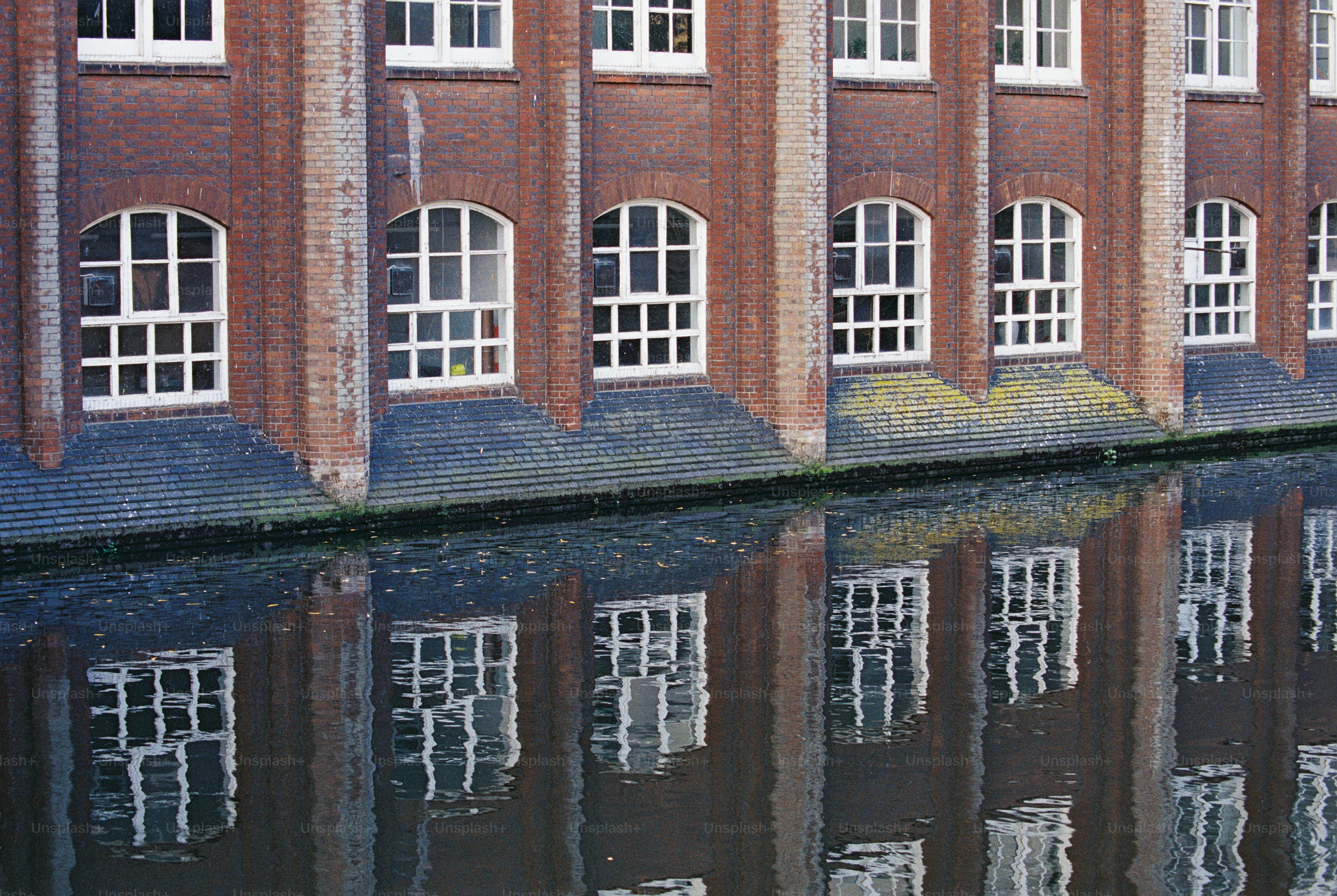 Red brick building reflecting in water - Photo on Unsplash+