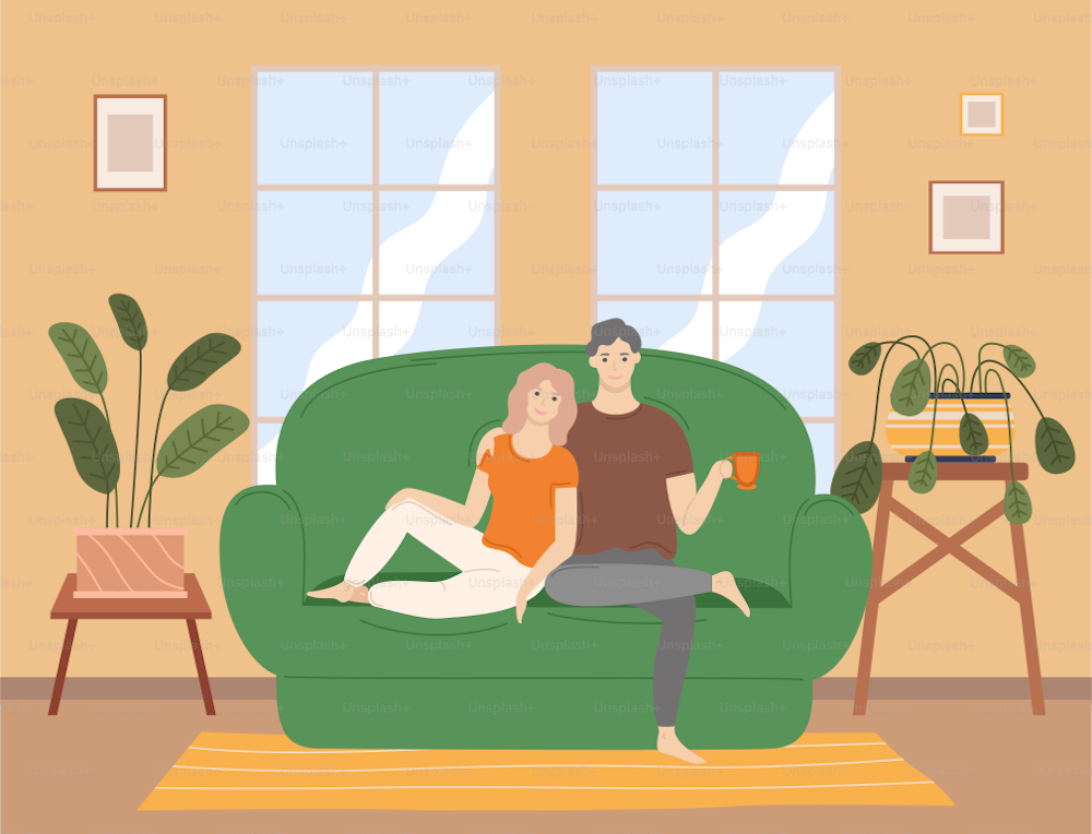Couple sitting on the couch at home in the living room interior near big window, drinking tea and talking. Family stay at home. Man and woman hugging each other. Young family spend time together