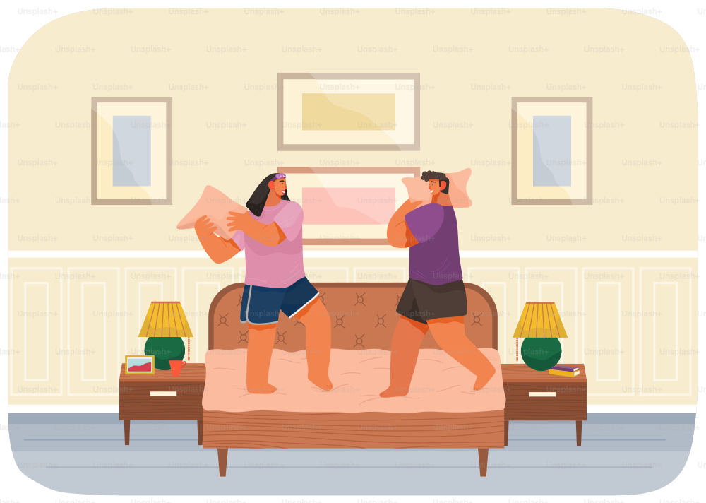 Young couple having pillow battle, man and woman wearing pajamas enjoying time together. Funny lovers beat with pillows standing on bed at home in modern apartment bedroom interior, happy family
